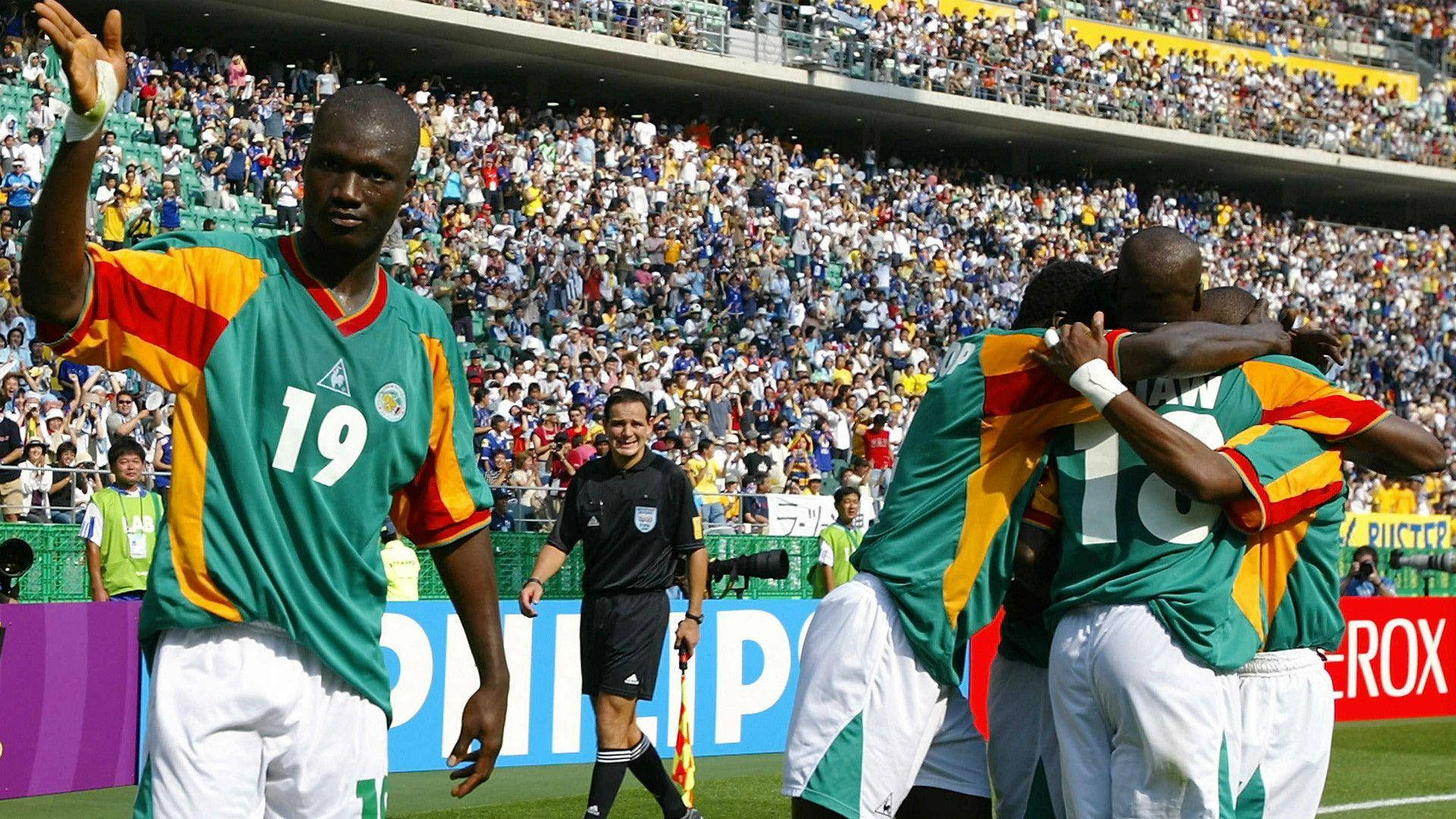 Senegal 桌布 壁紙 — 身穿綠色、黃色和紅色球衣的足球運動員在陽光明媚的球場上慶祝進球，看台上球迷歡呼雀躍。