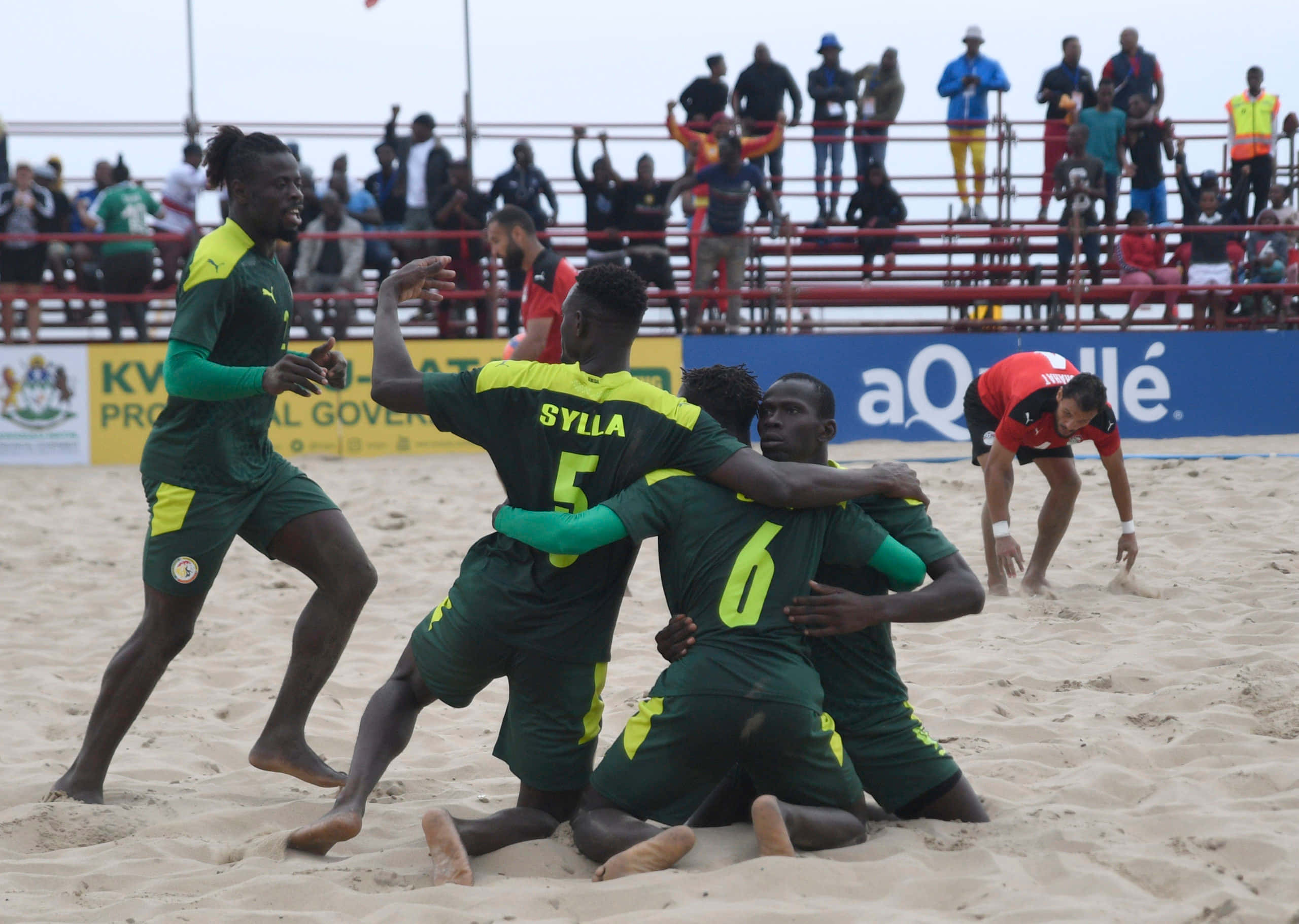 Beach Soccer 桌布 壁紙 — 身穿綠色和黃色球衣的沙灘足球運動員在沙地上慶祝進球，背景有觀眾。