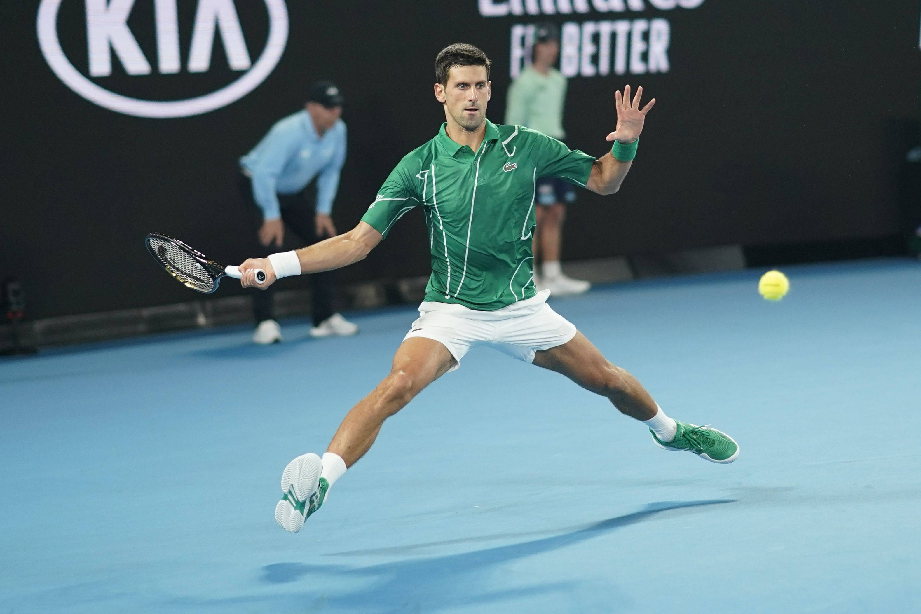 Australian Open 桌布 壁紙 — 身穿綠色球衣的網球選手在半空中飛身擊打藍色球場上的黃色球，燈光明亮。