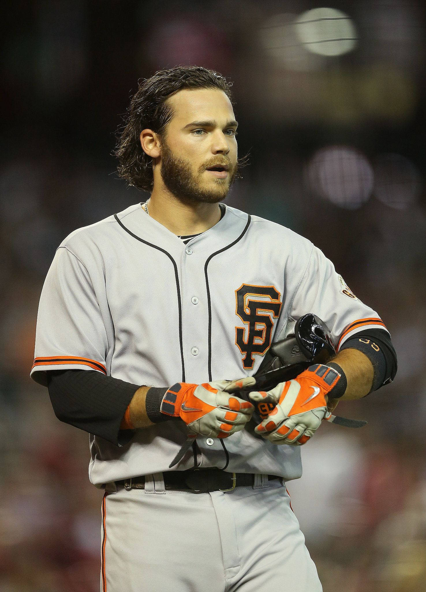 San Francisco Giants 桌布 壁紙 — 身穿舊金山巨人隊球衣的棒球運動員在夜間球場燈光下手持頭盔和手套。