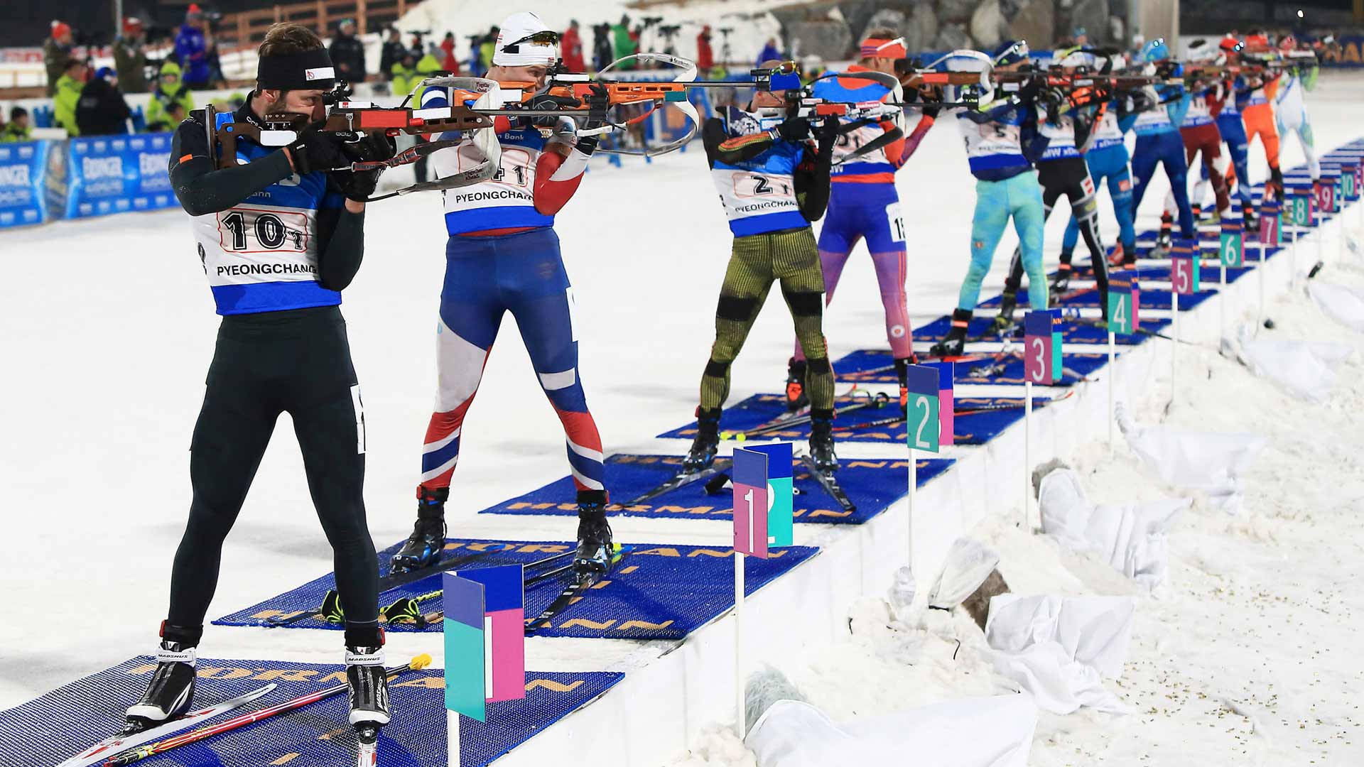 Olympics 桌布 壁紙 — 身穿色彩繽紛制服的冬季兩項運動員在冬季比賽期間，將步槍瞄準一個積雪的射擊場。
