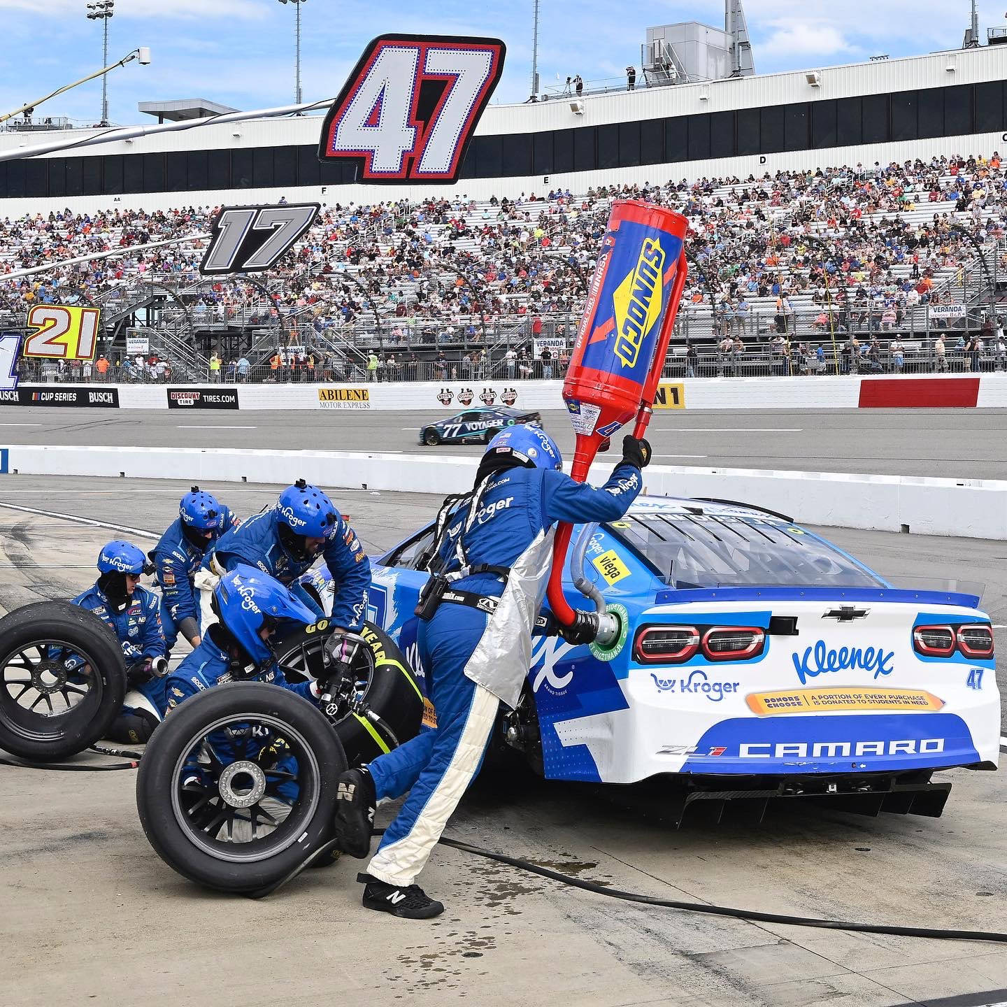 Racing 桌布 壁紙 — 身穿藍色制服的NASCAR維修站團隊在明亮的日光下的比賽中，快速更換藍白色#47雪佛蘭Camaro的輪胎。