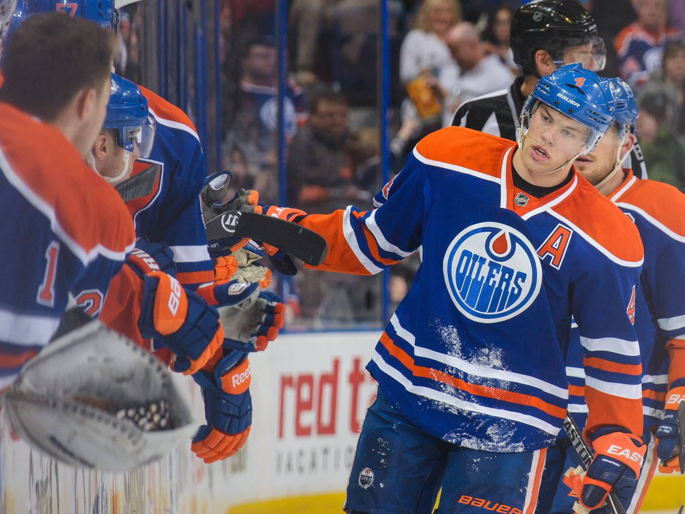 hockey 桌布 壁紙 — 身穿藍色和橙色Oilers球衣的曲棍球球員在冰屑飛濺的板牆附近慶祝。
