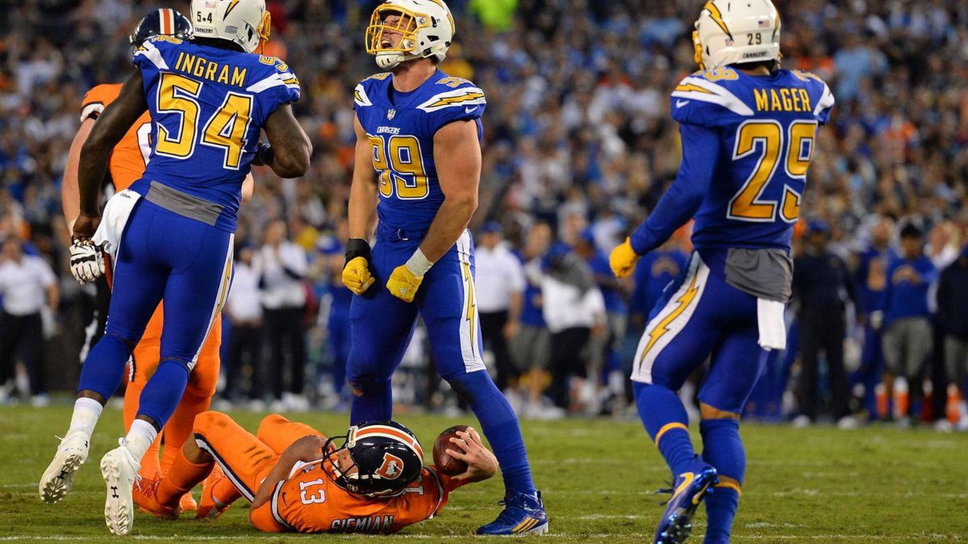 Football Players 桌布 壁紙 — 身穿藍色和橙色球衣的足球運動員在體育場燈光下，於充滿活力的綠色球場上慶祝達陣。