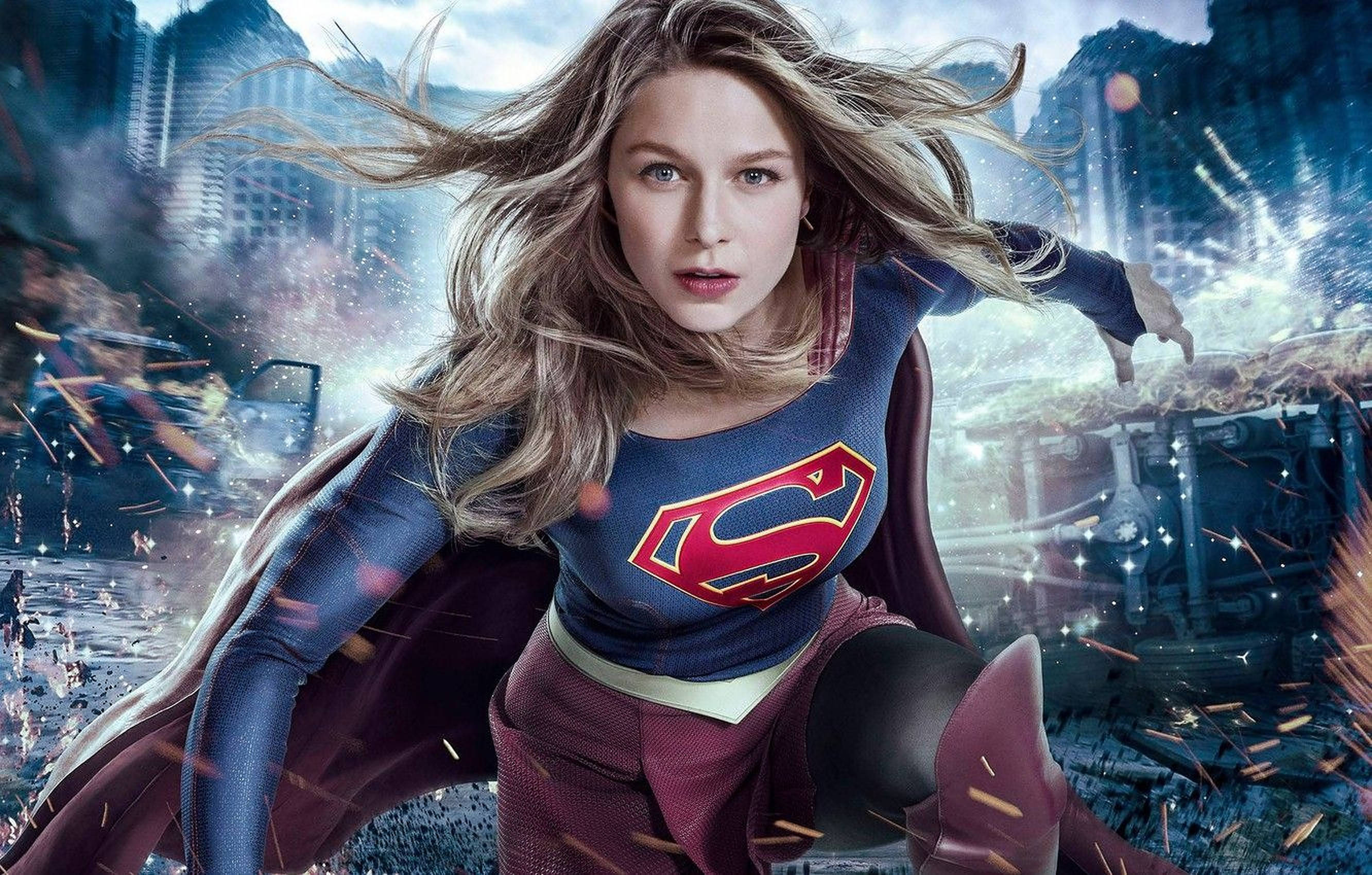 Superwoman 桌布 壁紙 — 身穿藍色和紅色套裝的超級女英雄穿過破碎的城市景觀，周圍有碎片飛舞。