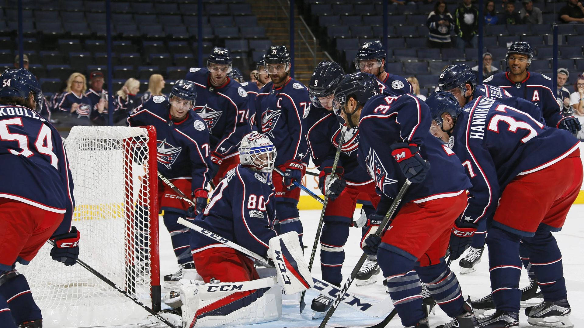 Columbus Blue Jackets 桌布 壁紙 — 身穿藍色和紅色球衣的曲棍球運動員在激烈的比賽中聚集在球門周圍，背景有球迷。