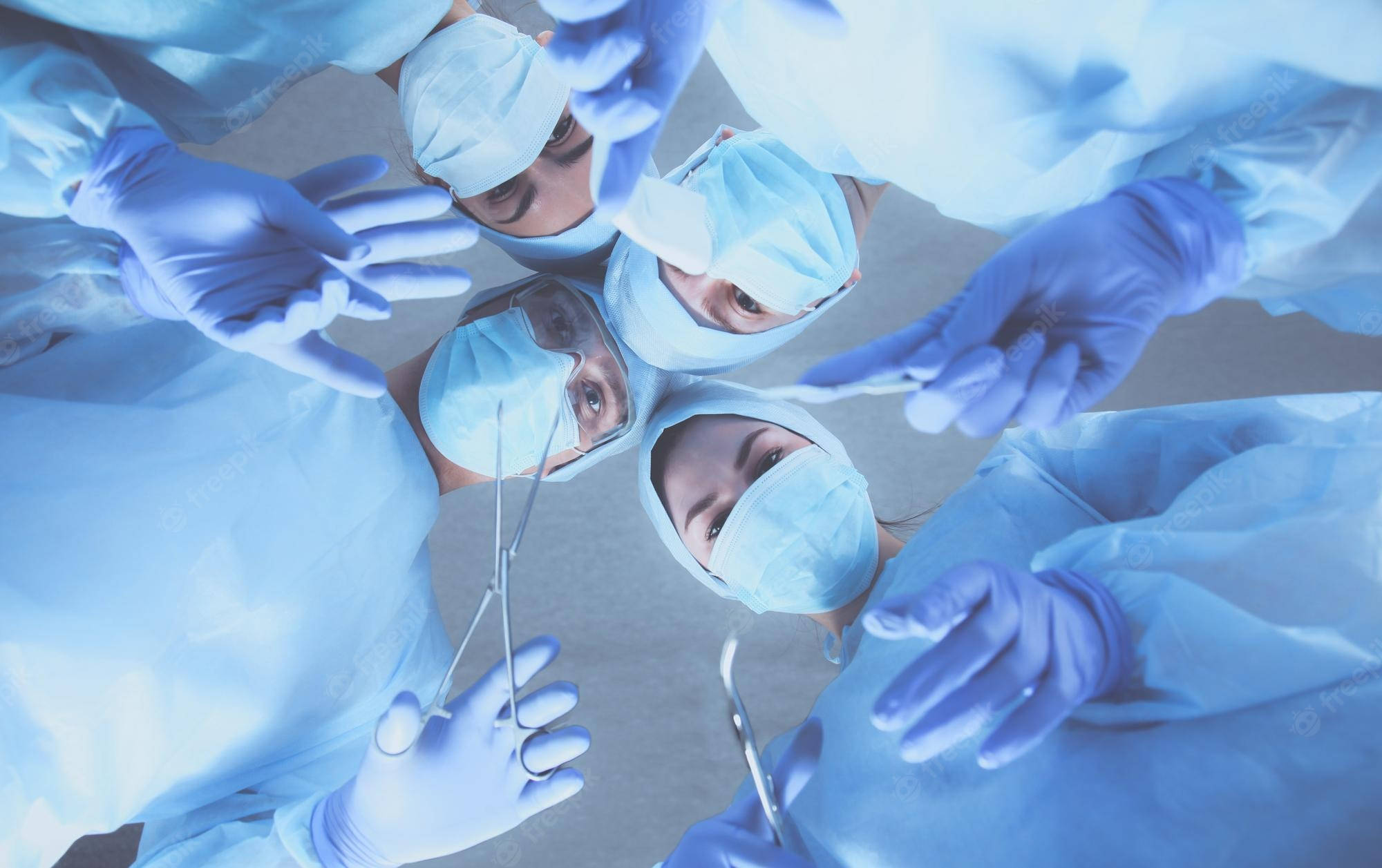 Medical 桌布 壁紙 — 身穿藍色手術服和手套的外科醫生從上方緊密圍成一圈，專注於下方看不見的病人。