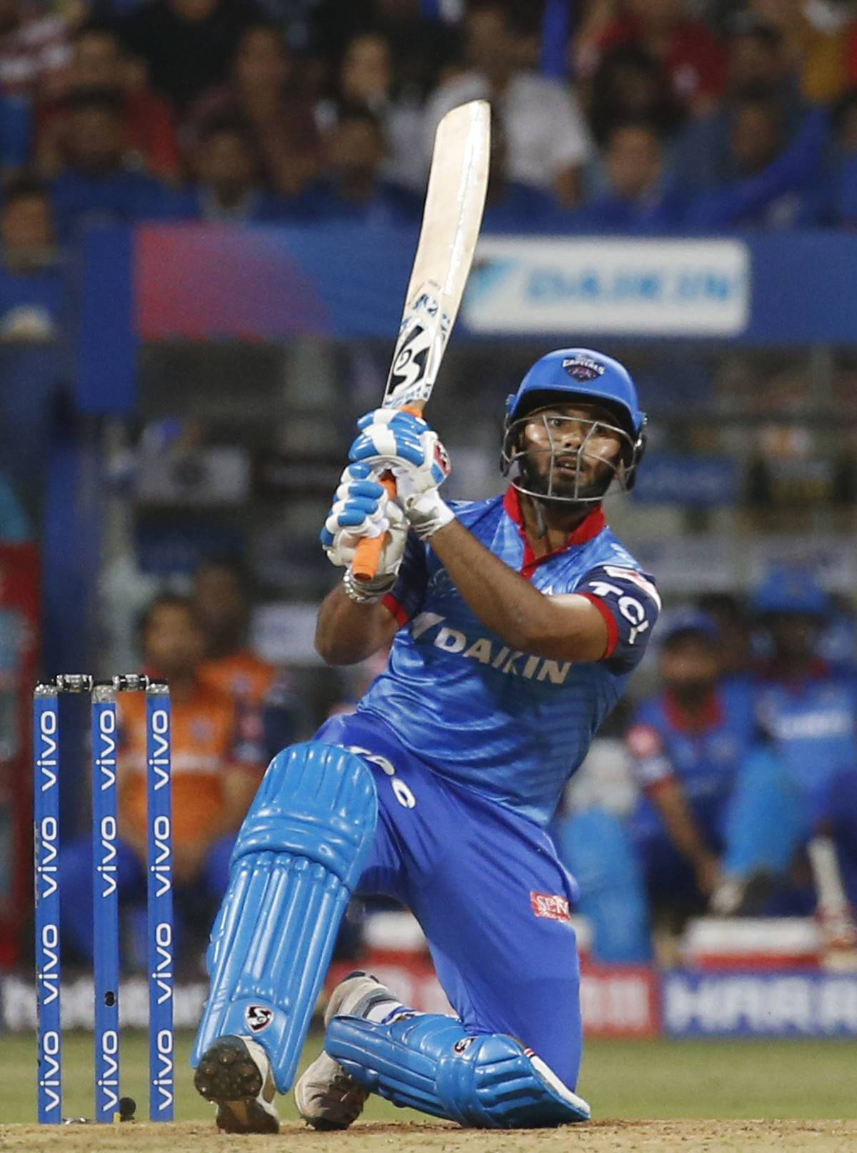 Delhi Capitals 桌布 壁紙 — 身穿藍色球衣的板球擊球手在夜間球場燈光下揮棒，背景是模糊的人群。