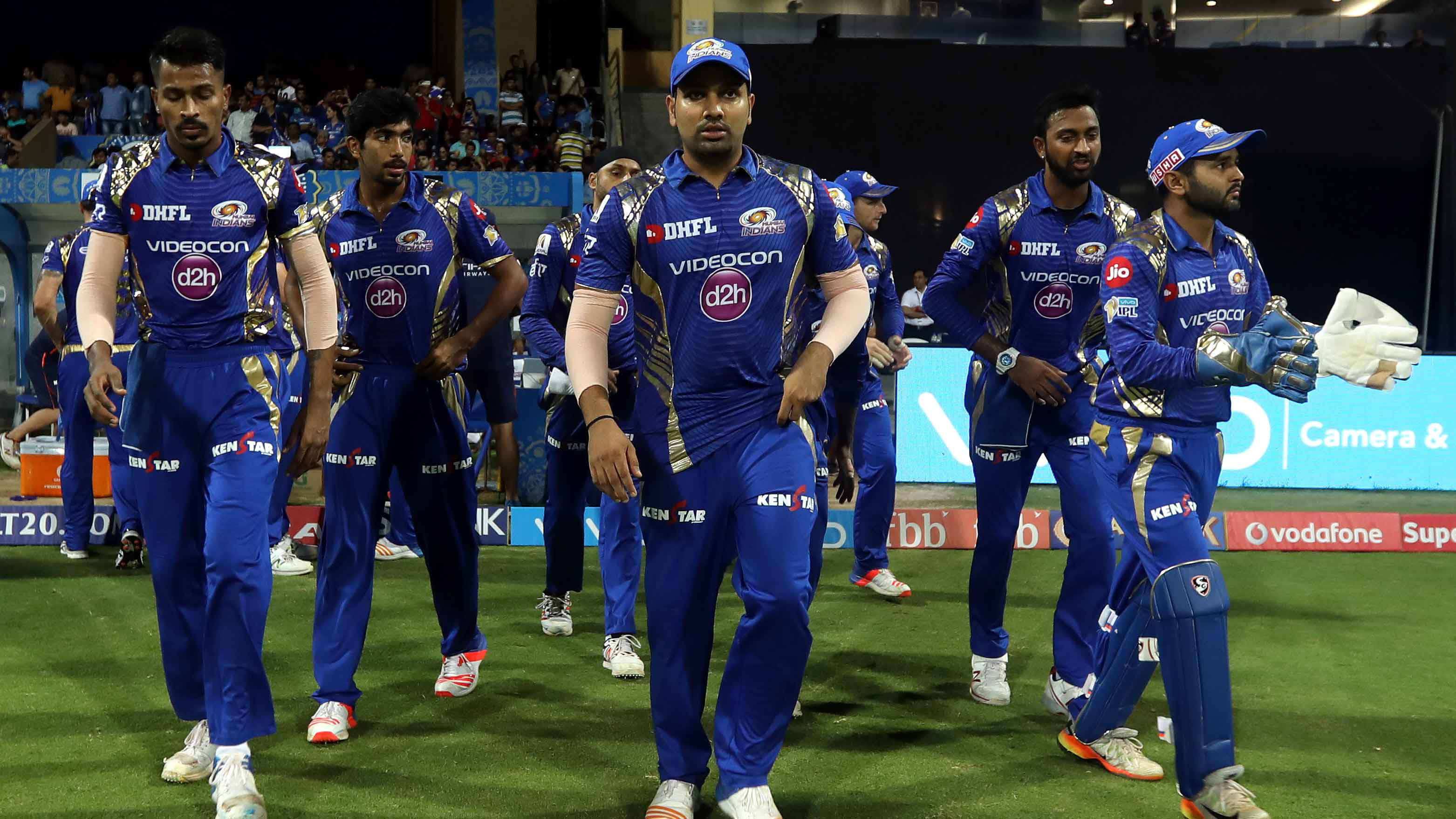 Mumbai Indians 桌布 壁紙 — 身穿藍色球衣的板球運動員在夜間比賽期間，在體育場燈光下走過綠色場地。