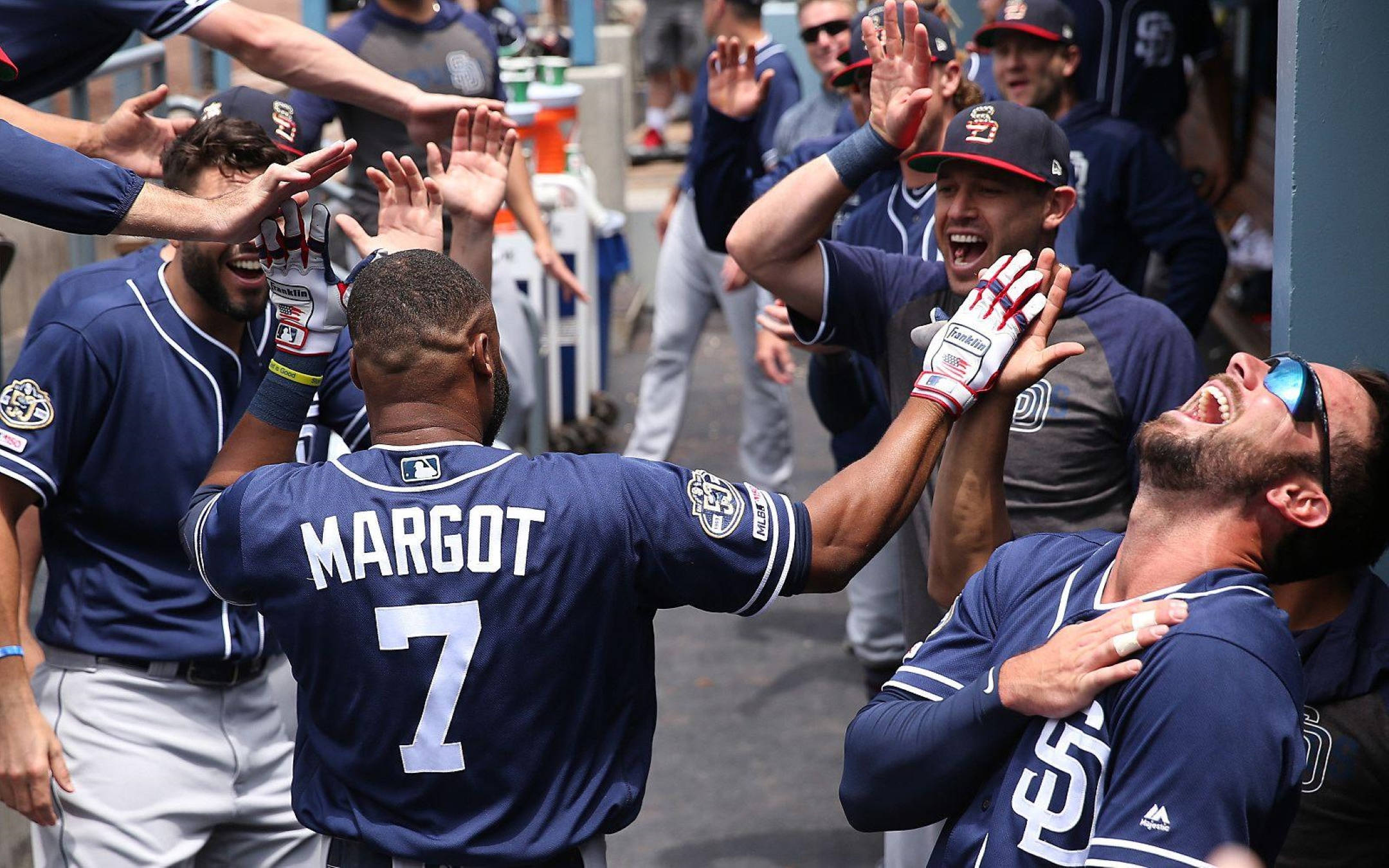 Padres 桌布 壁紙 — 身穿藍色球衣的棒球運動員在陽光普照的比賽中於休息區擊掌歡笑慶祝。