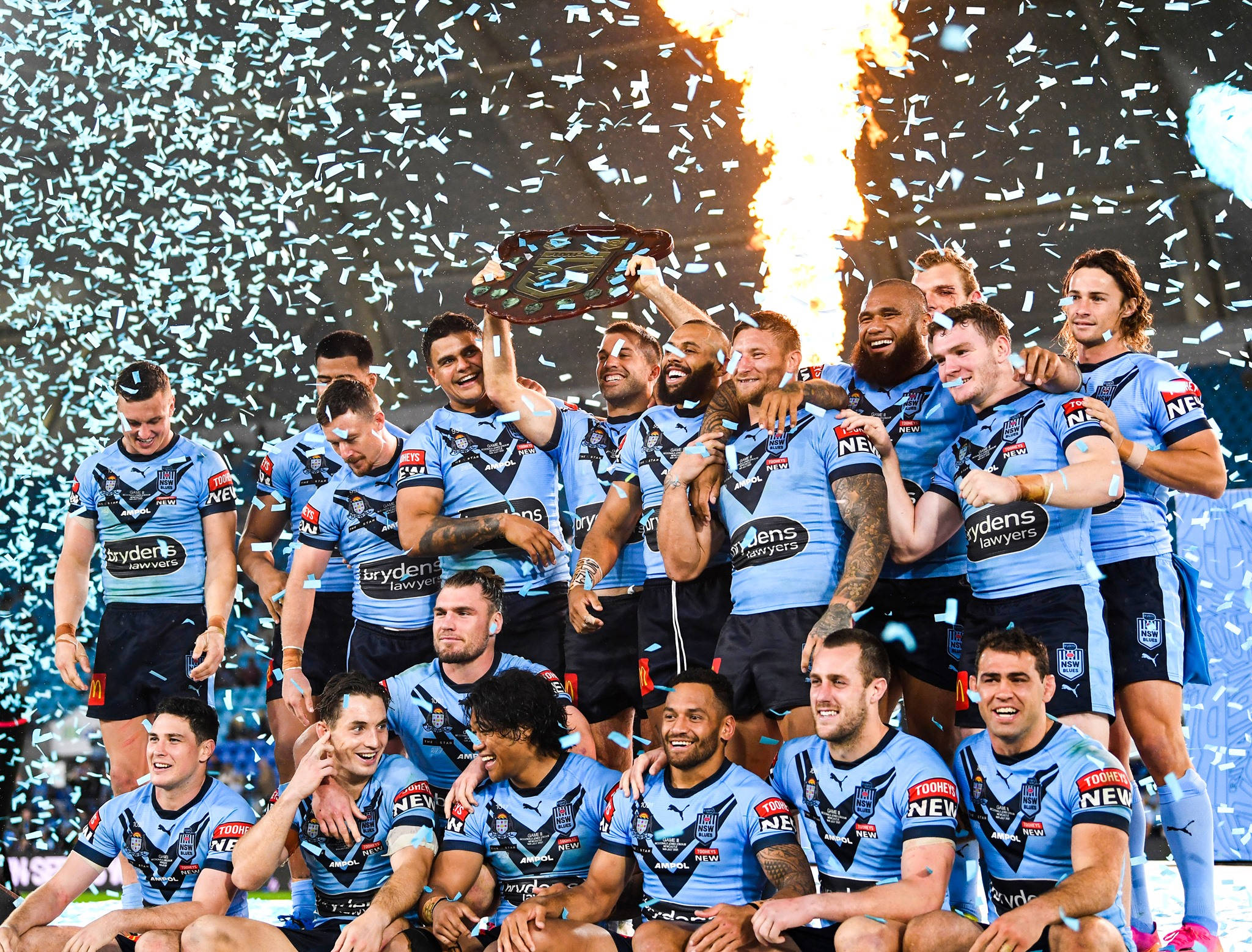 Nrl 桌布 壁紙 — 身穿藍色球衣的橄欖球聯賽球員在彩紙和火焰在背後爆發時，舉起獎盃慶祝勝利。