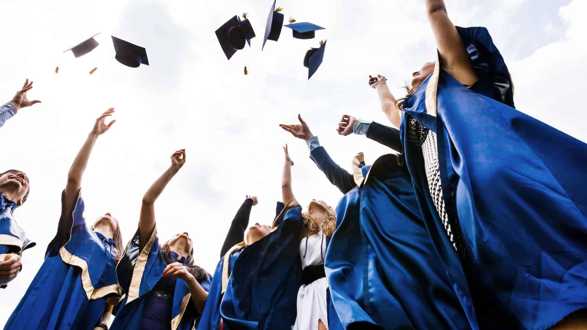 Graduation 桌布 壁紙 — 身穿藍色畢業帽和袍的畢業生們，在明亮的天空下歡快地將帽子拋向空中。