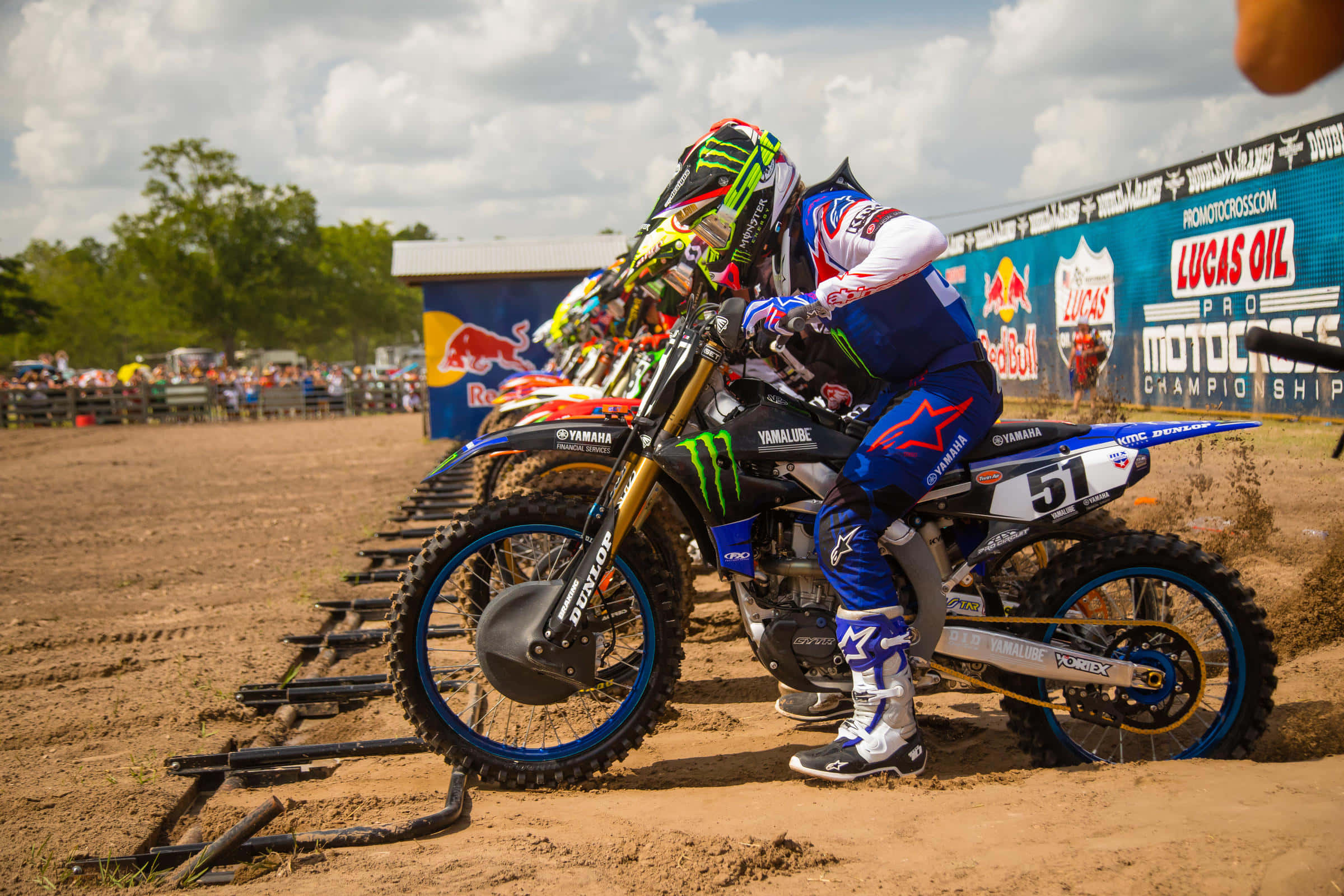 Motocross 桌布 壁紙 — 身穿藍色裝備的越野機車騎士在泥地賽道上傾斜過彎，背景有觀眾和贊助商橫幅。