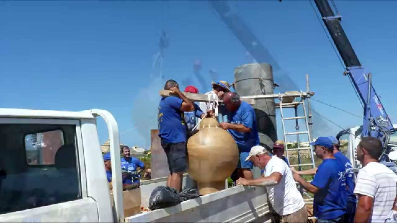 Malta 桌布 壁紙 — 身穿藍色襯衫的工人在晴朗的藍天下將一個大型米色陶瓷容器抬到白色卡車上，背景有起重機。