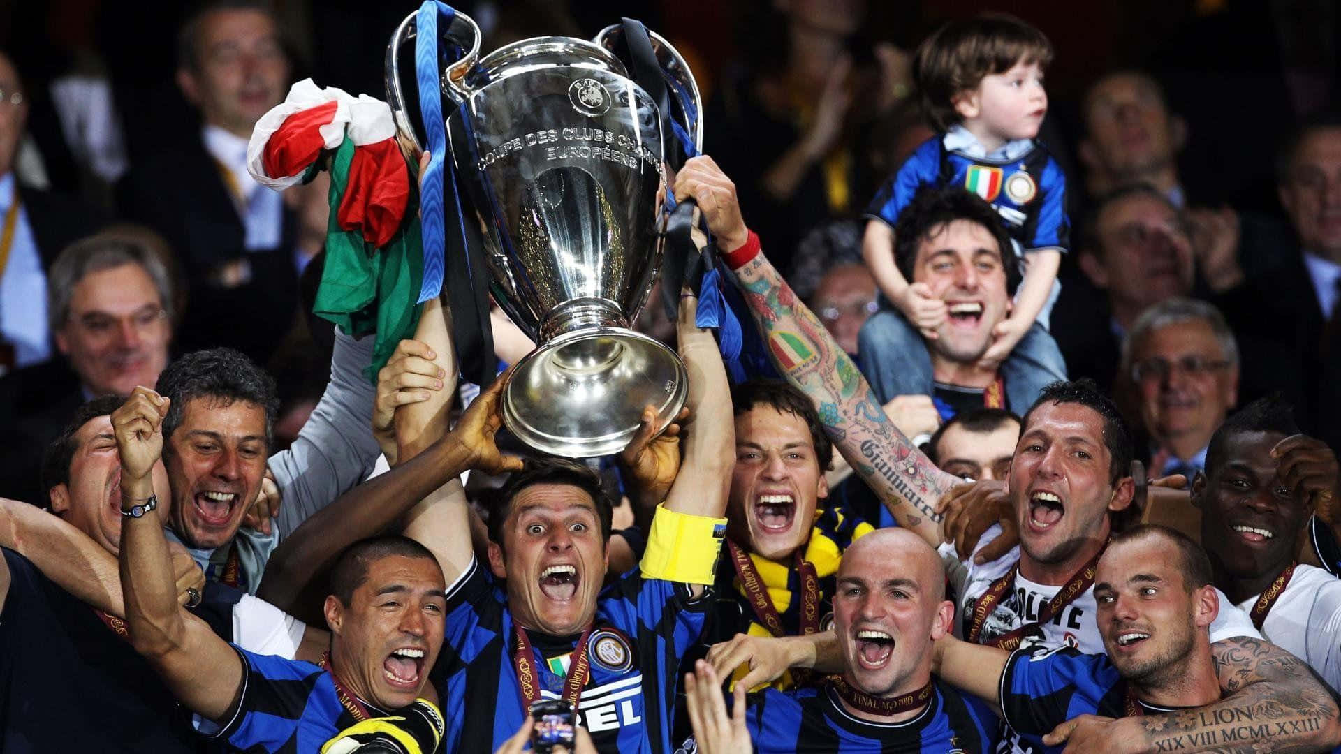 Inter Milan 桌布 壁紙 — 身穿藍黑條紋球衣的足球運動員在體育場人群中歡欣鼓舞地將閃亮的銀色獎盃高舉過頭頂。