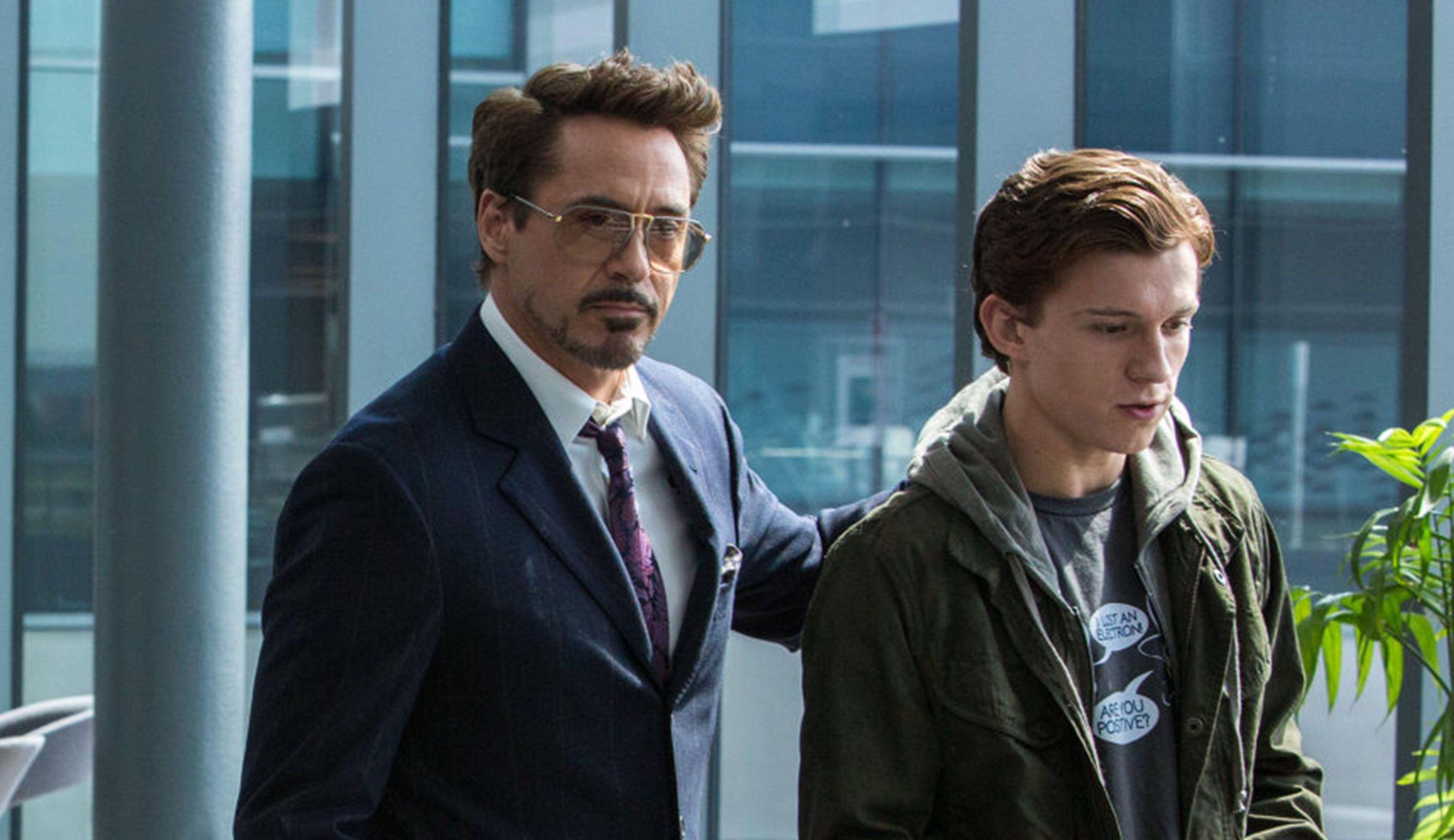 Peter Parker 桌布 壁紙 — 身穿西裝的東尼史塔克將手放在年輕彼得帕克的肩膀上，他們正走過一座現代玻璃建築。