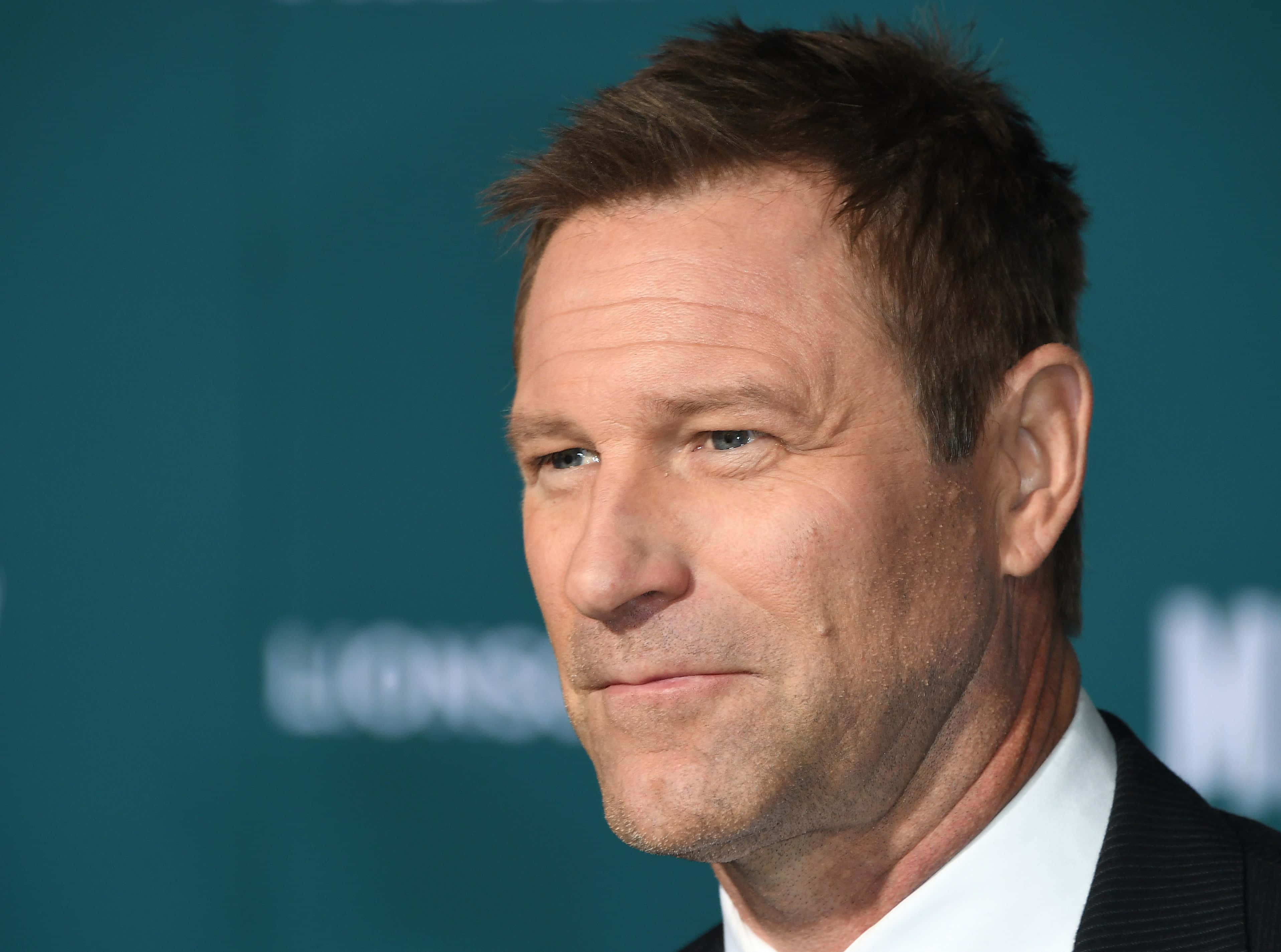 Celebrity 桌布 壁紙 — 身穿西裝的男士特寫肖像，表情嚴肅，背景為青綠色。