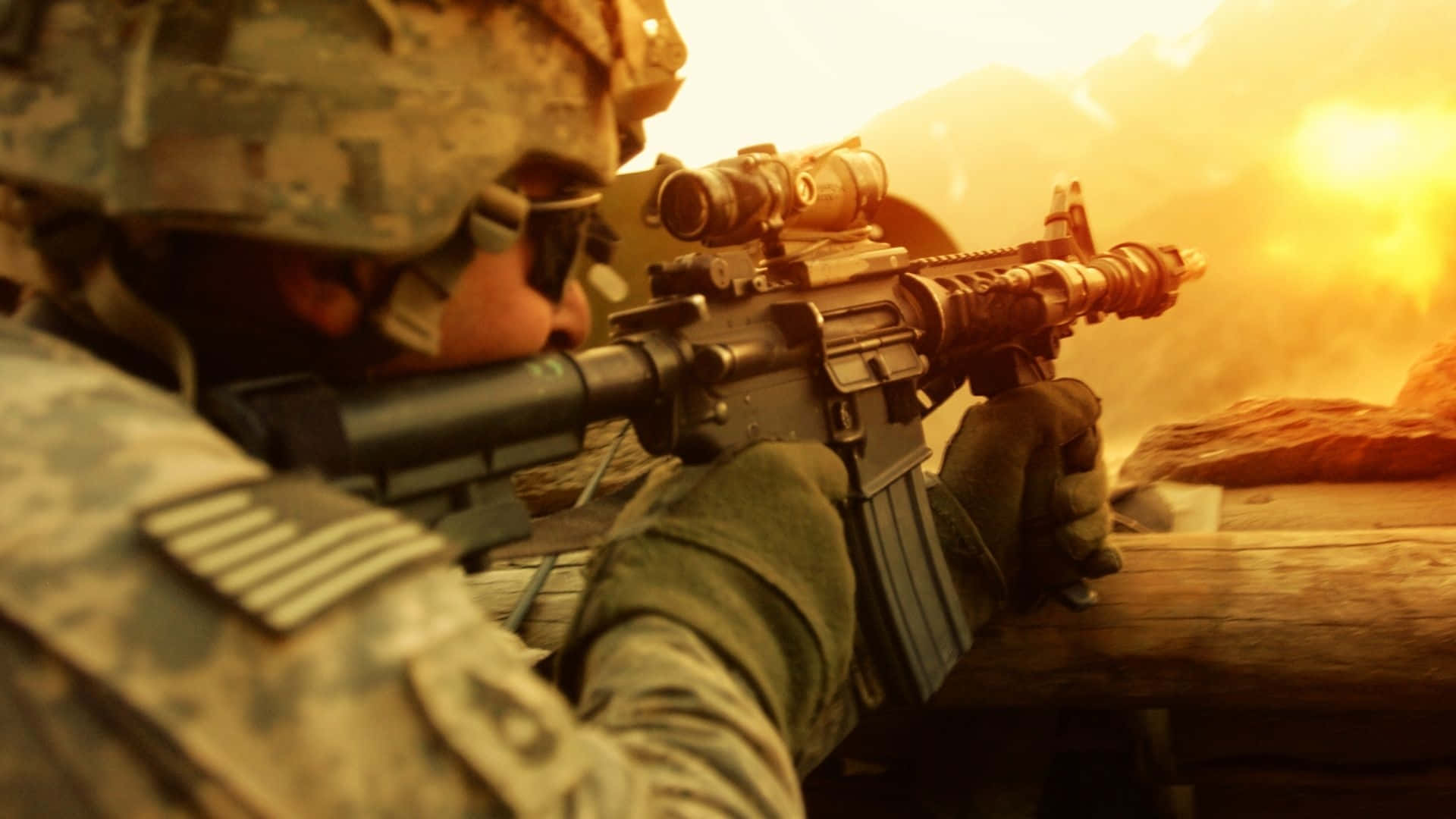 軍隊 桌布 壁紙 — 身穿迷彩服的士兵以俯臥姿勢瞄準步槍，背後爆炸照亮塵土飛揚的戰場。