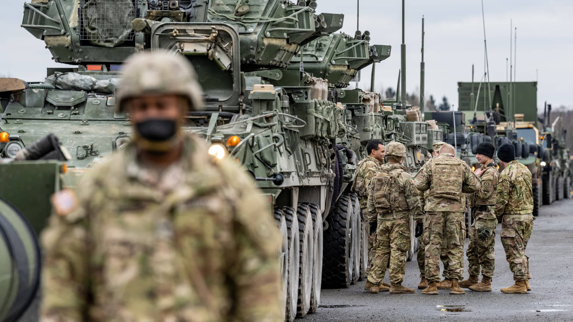  壁紙 — 身穿迷彩服的士兵站在一排長長的橄欖綠軍用裝甲車旁，天空多雲。