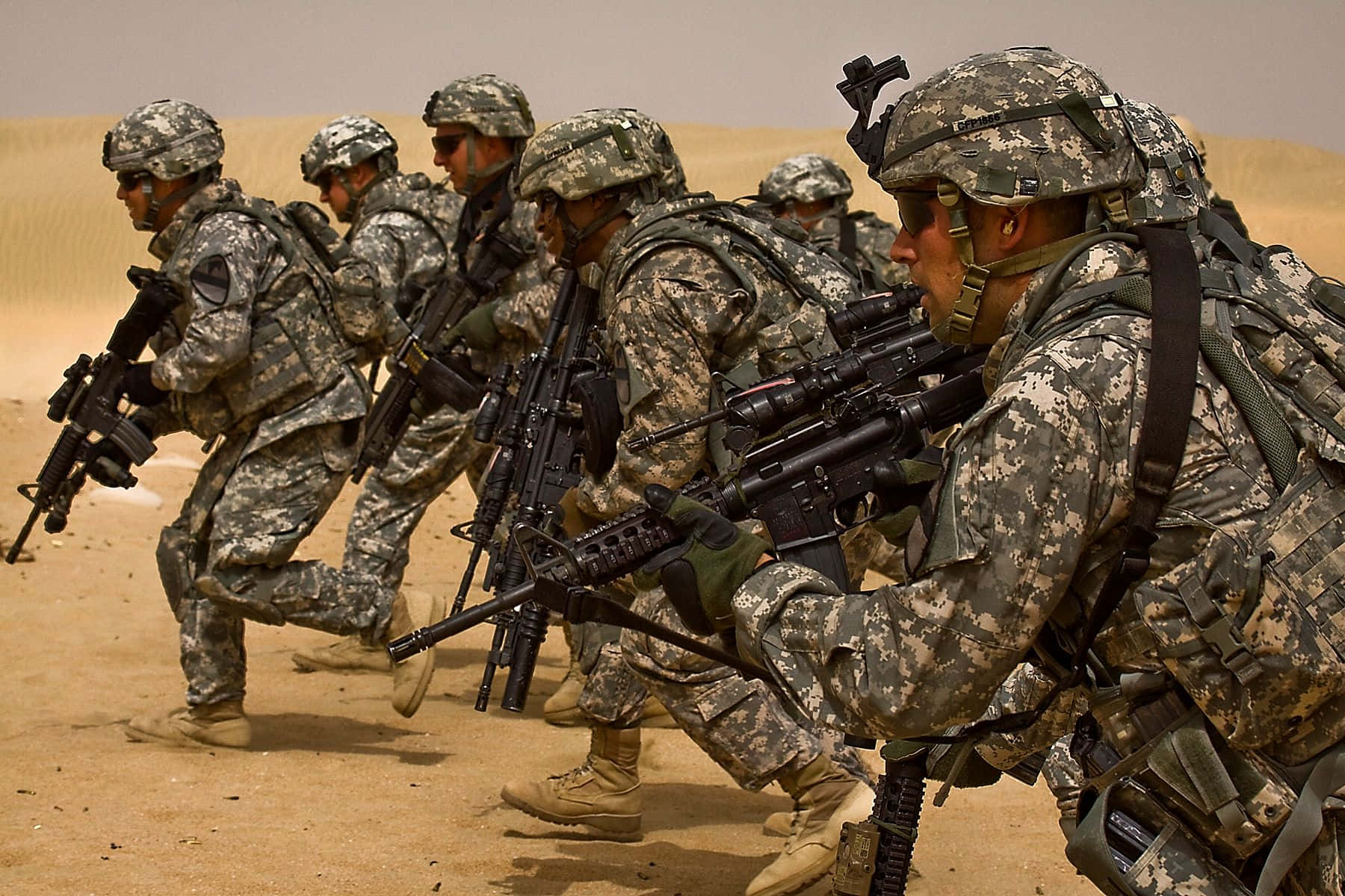 軍隊 桌布 壁紙 — 身穿迷彩裝備的士兵在朦朧的天空下以沙漠隊形前進，手持步槍。