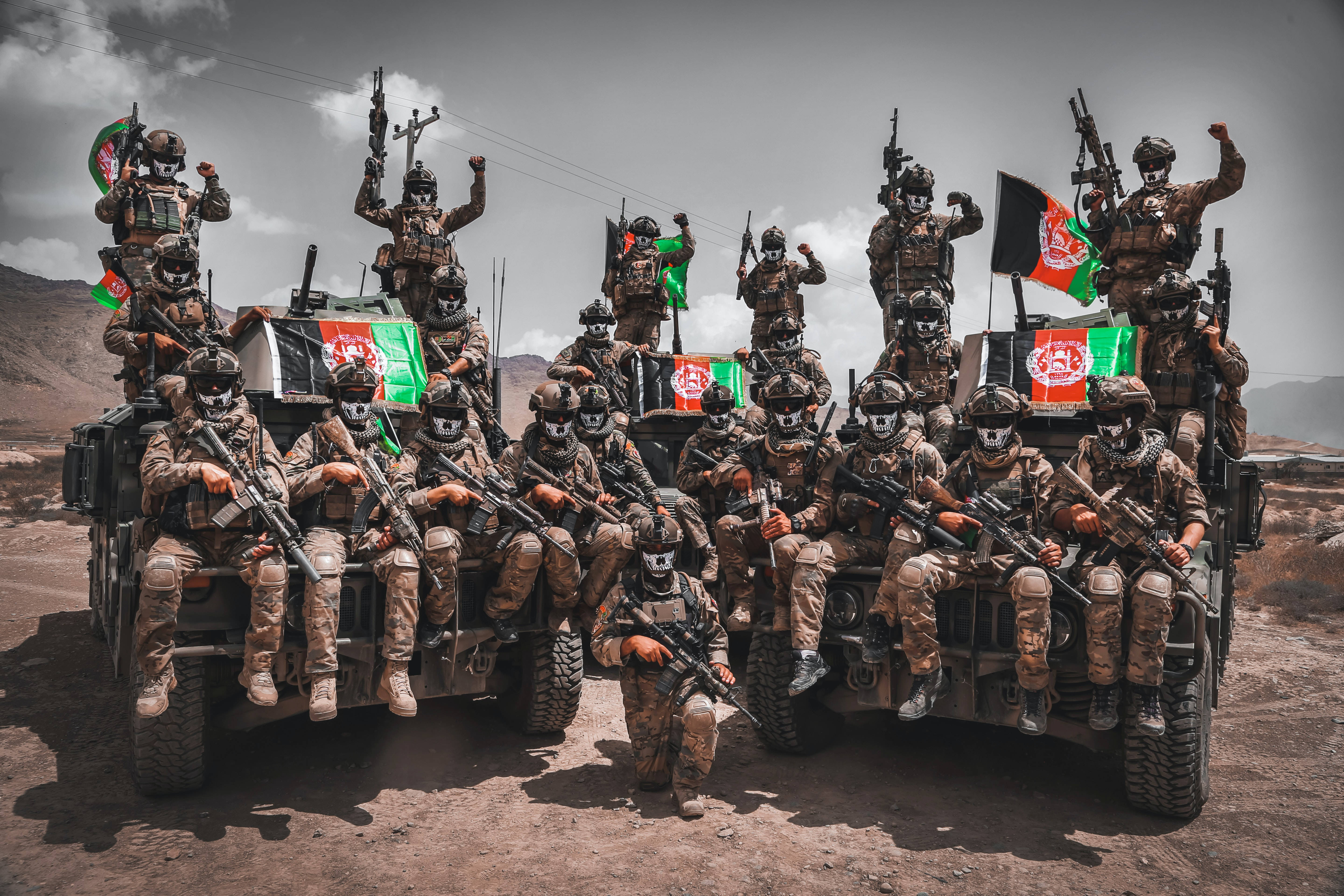 Kabul 桌布 壁紙 — 身穿迷彩裝備的士兵在裝甲車上擺出勝利姿態，在塵土飛揚的沙漠景觀中揮舞阿富汗國旗。