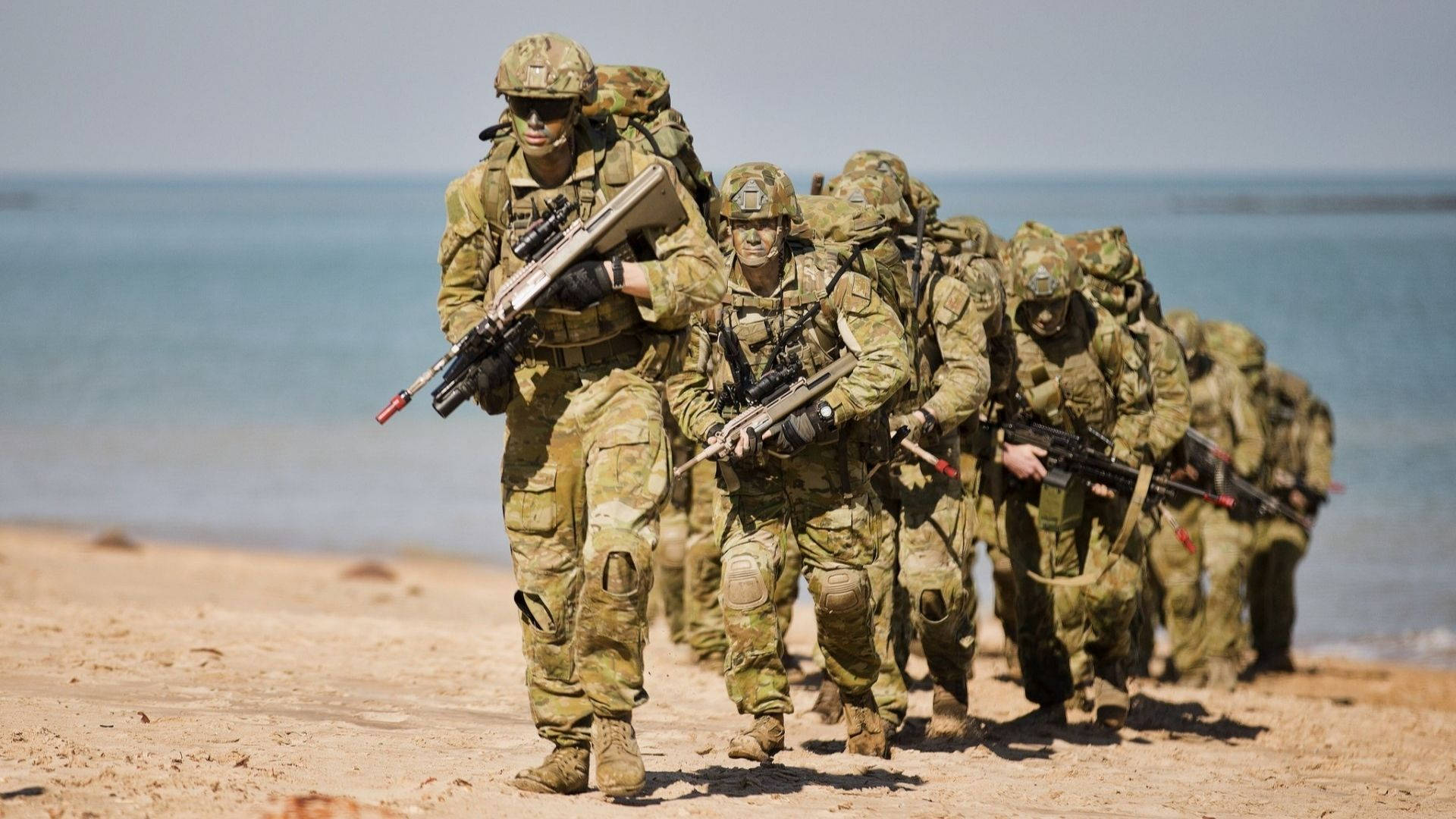 一排武裝士兵在靠近海洋的沙灘上行進。