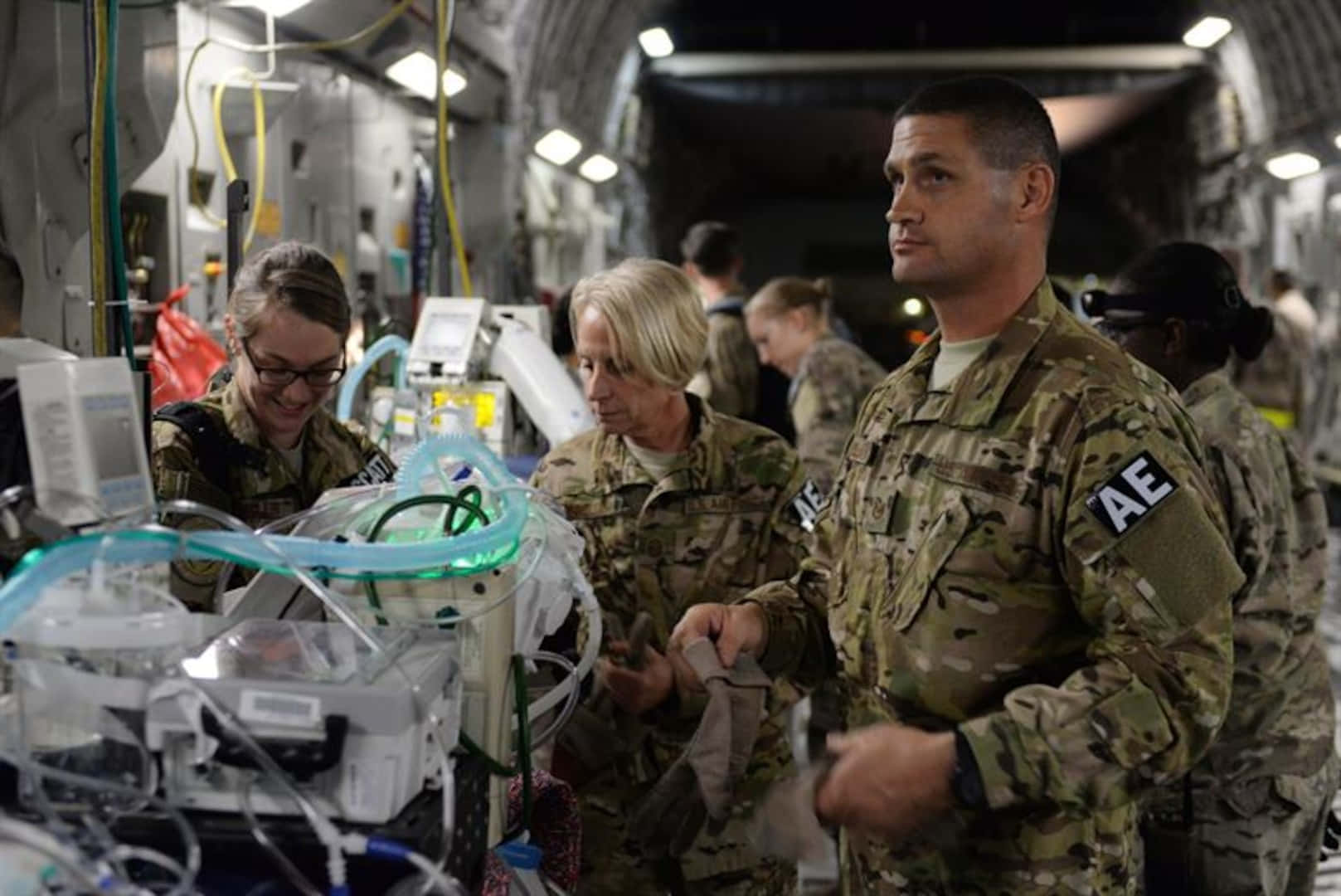 Air Force 桌布 壁紙 — 身穿迷彩軍服的軍醫在燈光昏暗的飛機貨艙內照顧使用呼吸器的病人。