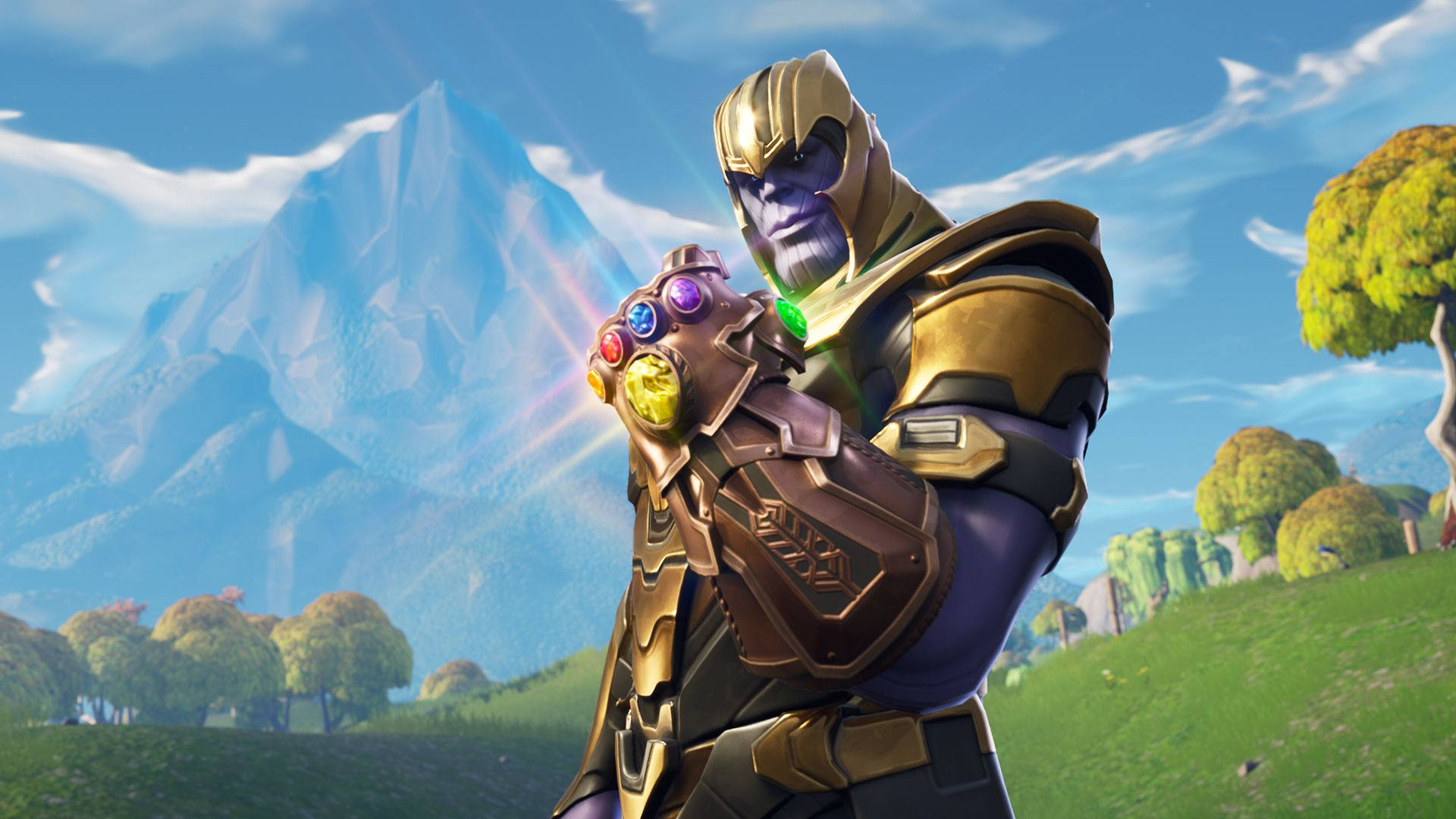 Fortnite 桌布 壁紙 — 身穿金色盔甲的薩諾斯站在長滿草的山丘上，手持發光的無限手套，背景是山脈和樹木，天空湛藍。