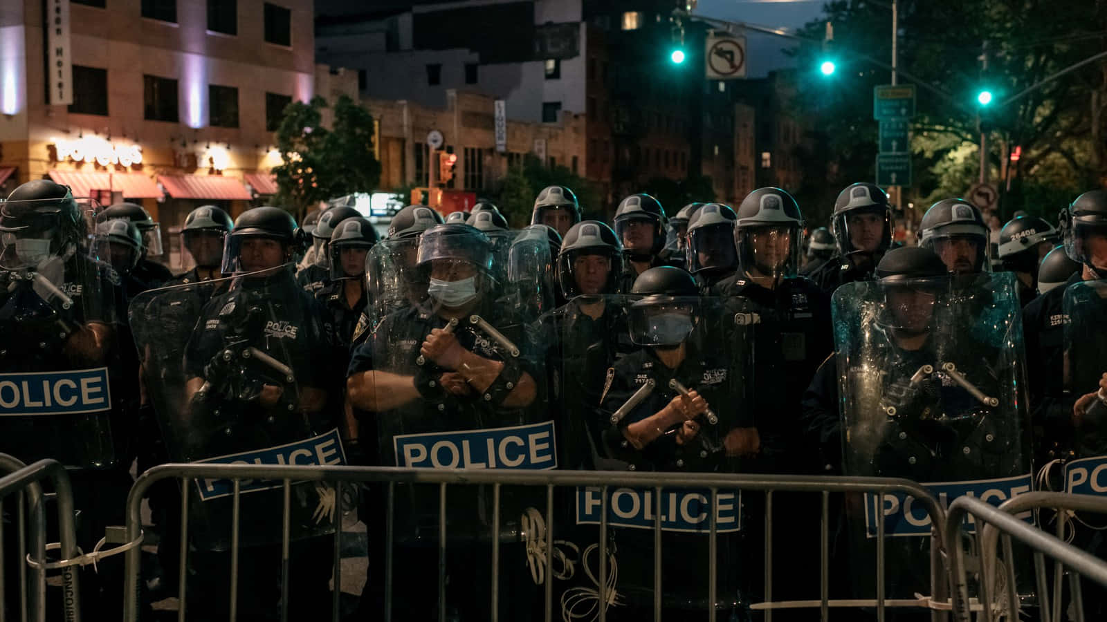 警察 桌布 壁紙 — 身穿防暴裝備的警察在夜間於城市街道上，手持盾牌和警棍，在路障後方列隊。