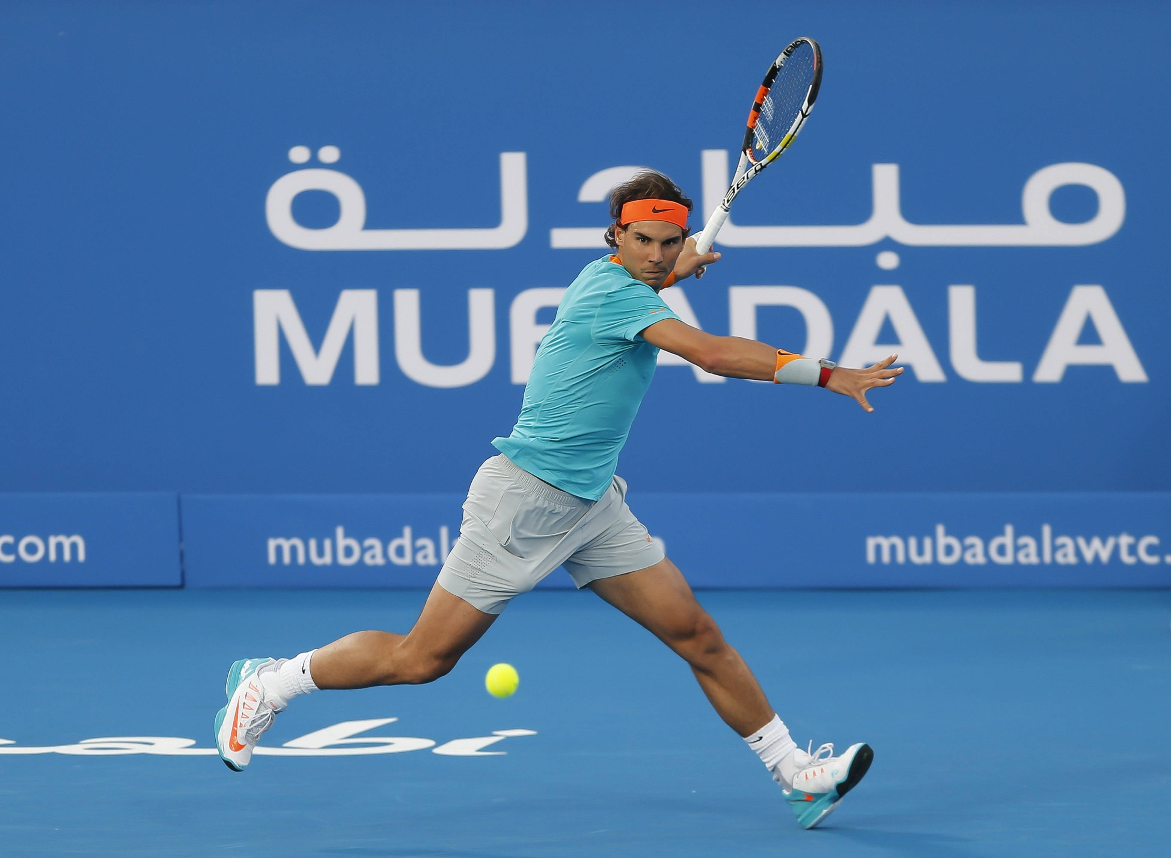 Rafael 桌布 壁紙 — 身穿青綠色襯衫的網球選手在帶有Mubadala標誌的鮮豔藍色球場上撲身擊打黃色球。