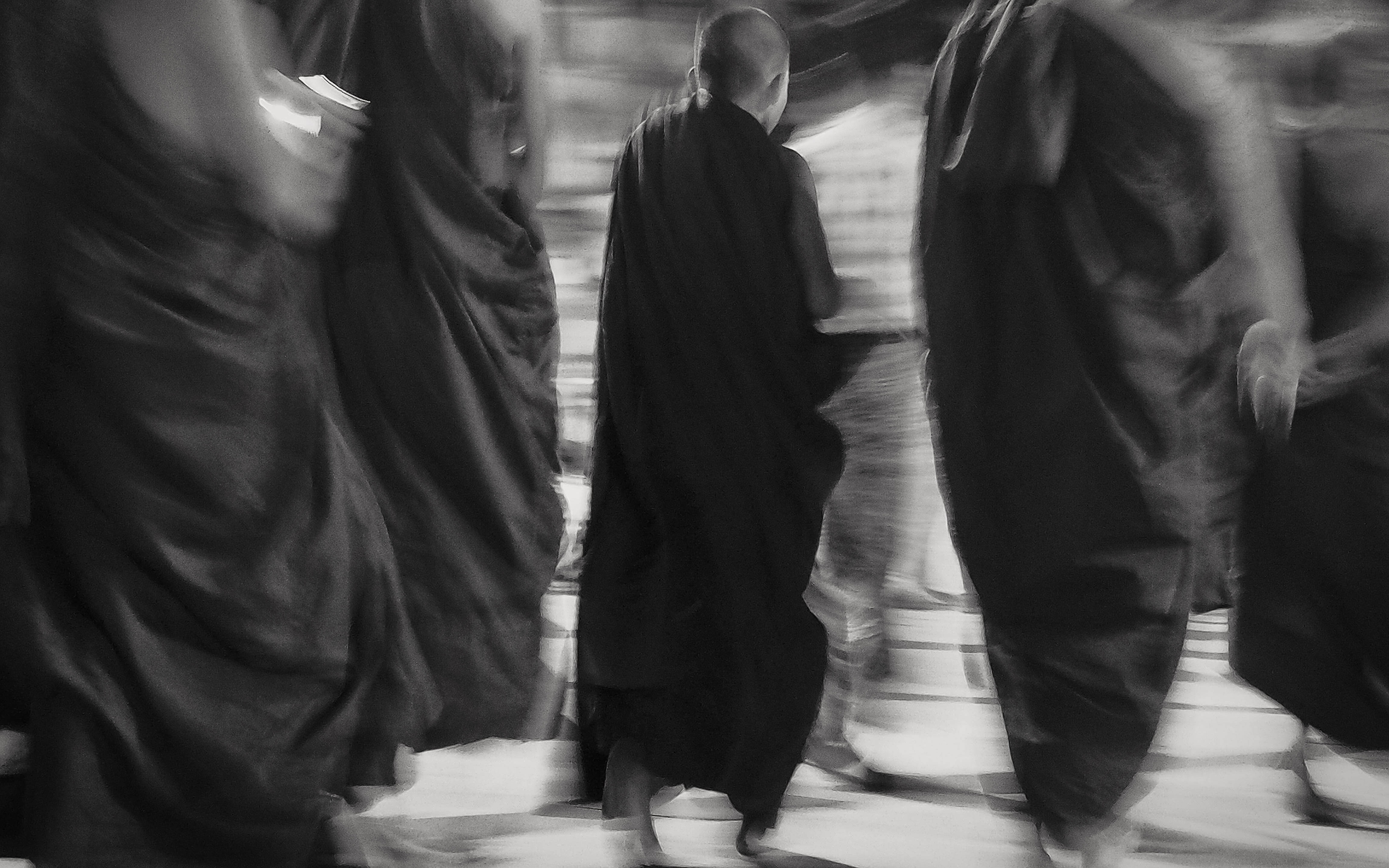 Yangon 桌布 壁紙 — 身穿飄逸長袍的僧侶以動態模糊的方式走過寧靜的寺廟庭院，呈現單色調。