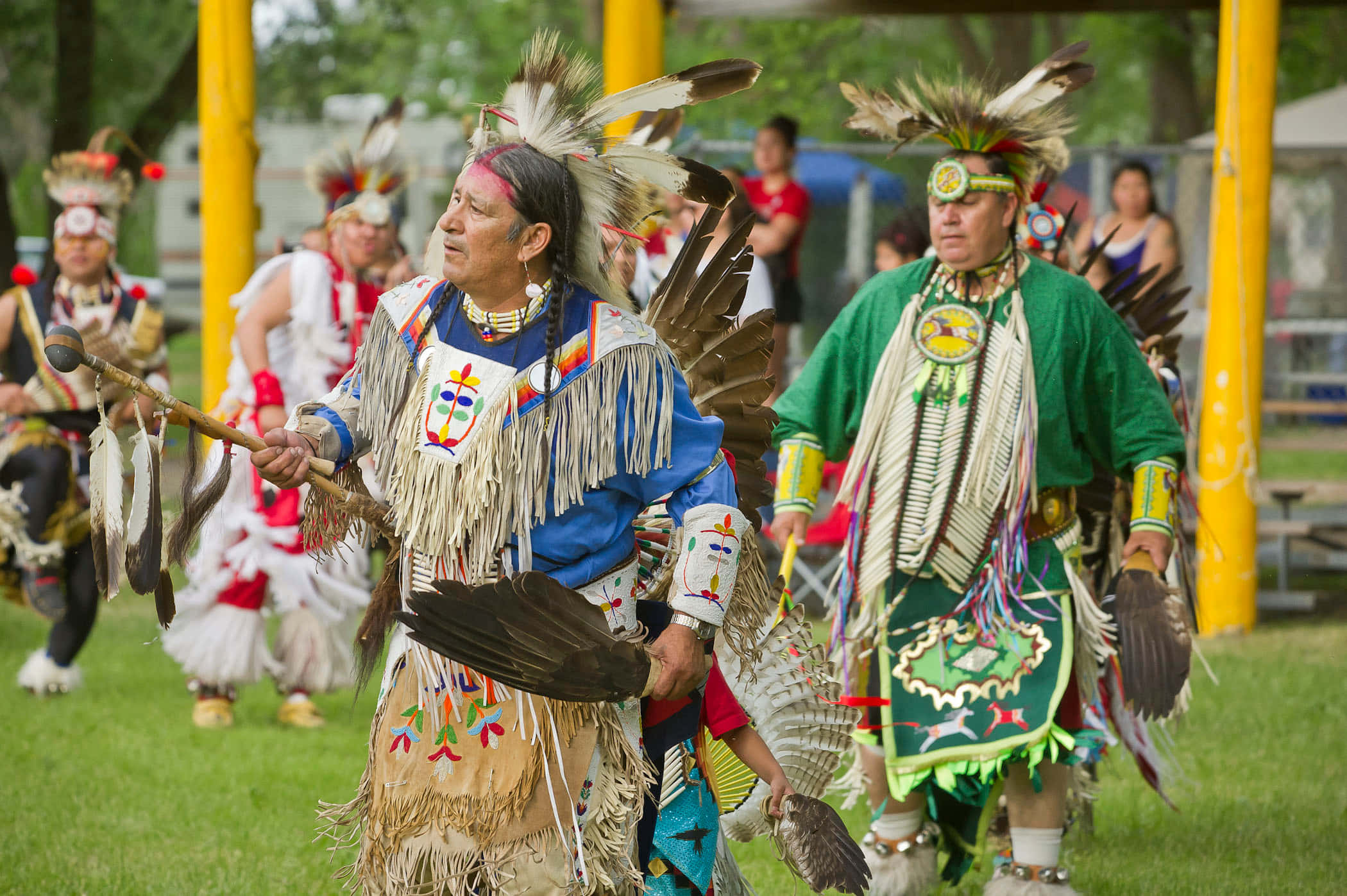 Native American 桌布 壁紙 — 身穿鮮豔傳統服飾的美洲原住民舞者在白天的草地上進行儀式舞蹈。