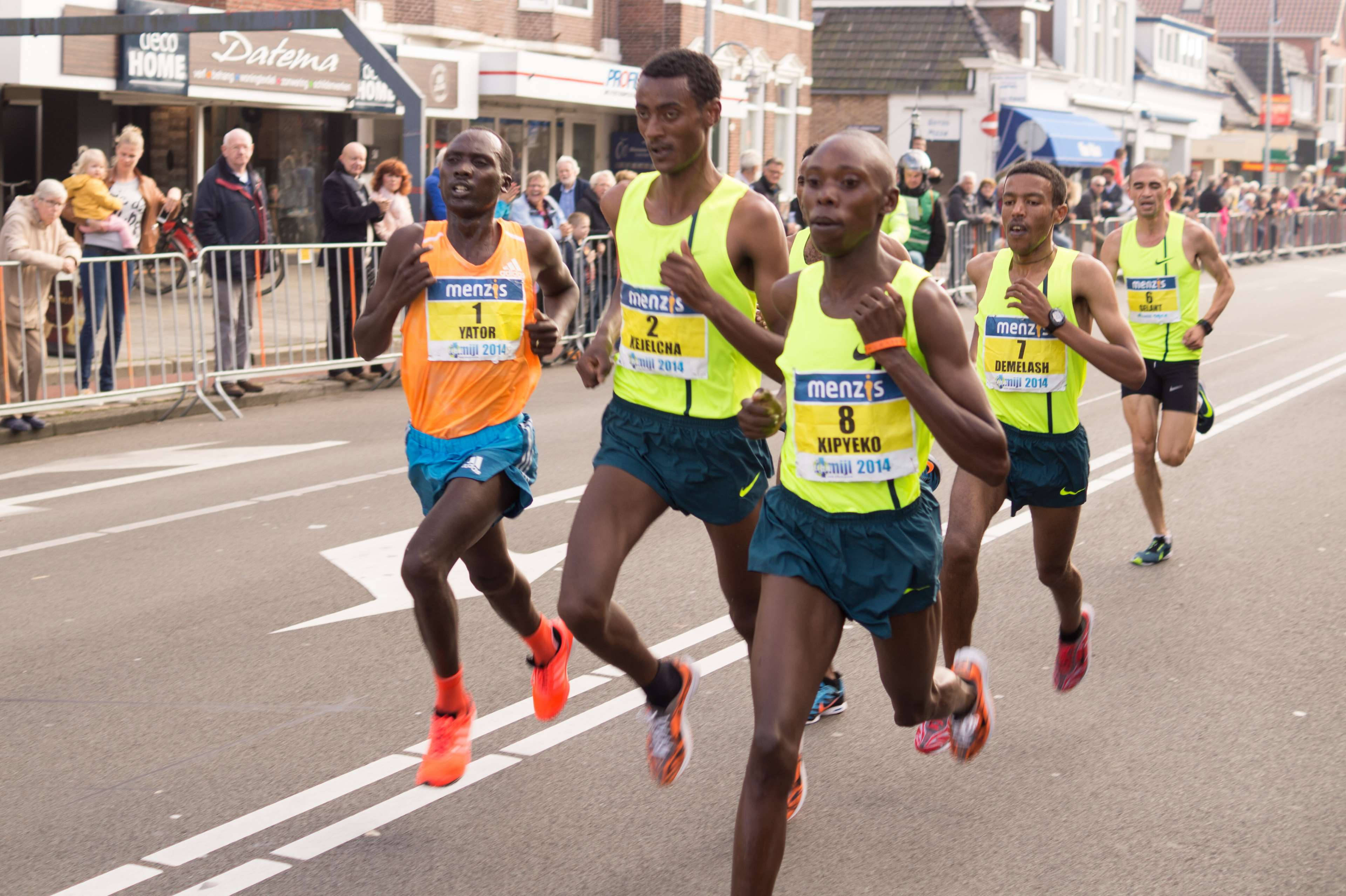 Marathon 桌布 壁紙 — 身穿鮮豔螢光背心的競技男跑者在街道上衝刺，觀眾在圍欄後歡呼。