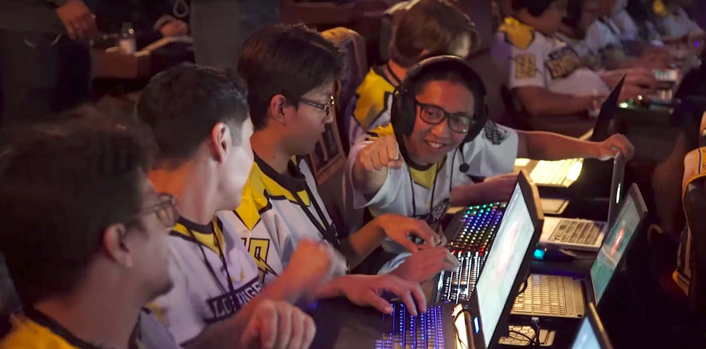 Esports 桌布 壁紙 — 身穿黃色和白色球衣的競技玩家在昏暗的場館燈光下，在發光的筆記型電腦上激烈地進行電競比賽。