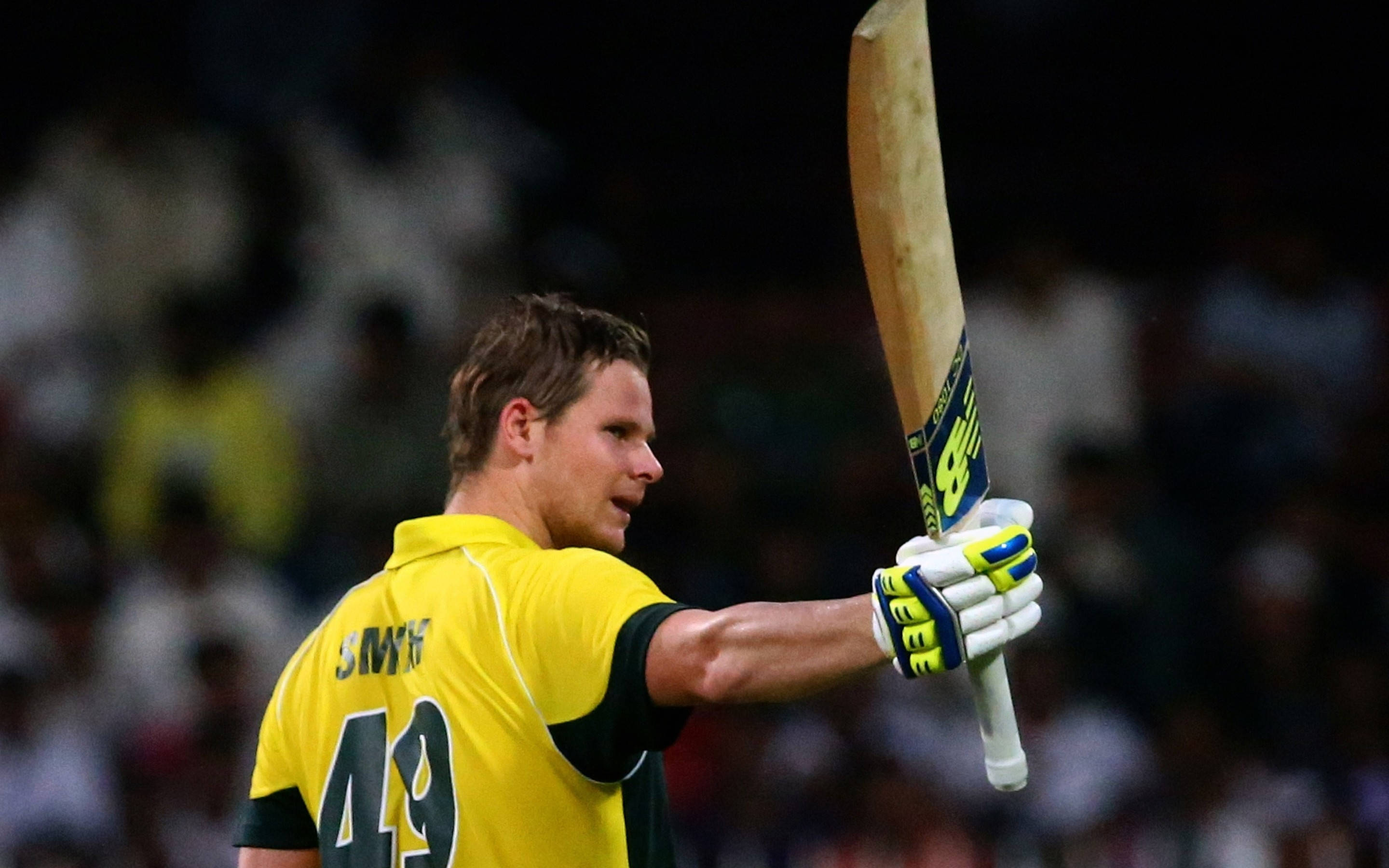 australia cricket 桌布 壁紙 — 身穿黃色球衣的板球運動員在球場燈光下高舉木製球拍慶祝勝利。