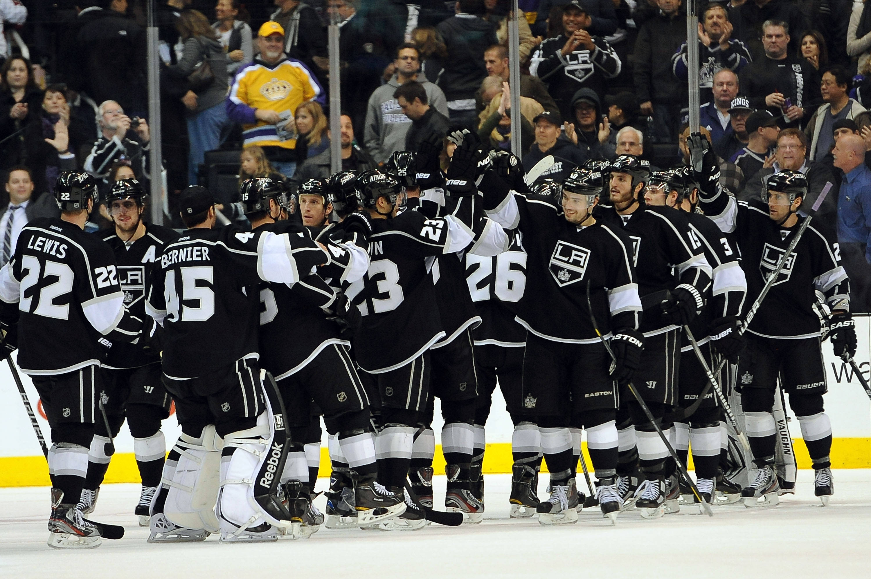 Los Angeles Kings 桌布 壁紙 — 身穿黑白球衣的曲棍球運動員在冰場上聚在一起，背景有球迷。