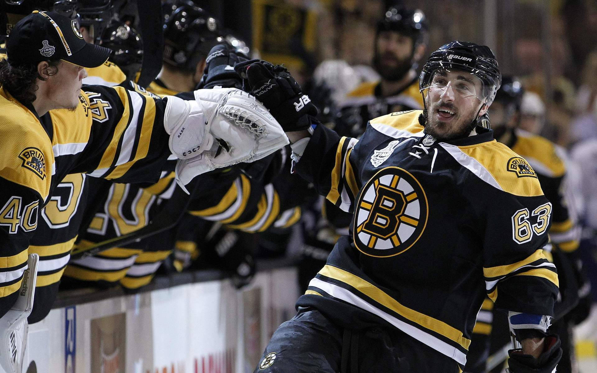 bruins 桌布 壁紙 — 身穿黑色和金色球衣的冰球運動員在冰上熱情慶祝，舉起手套，面露喜悅。