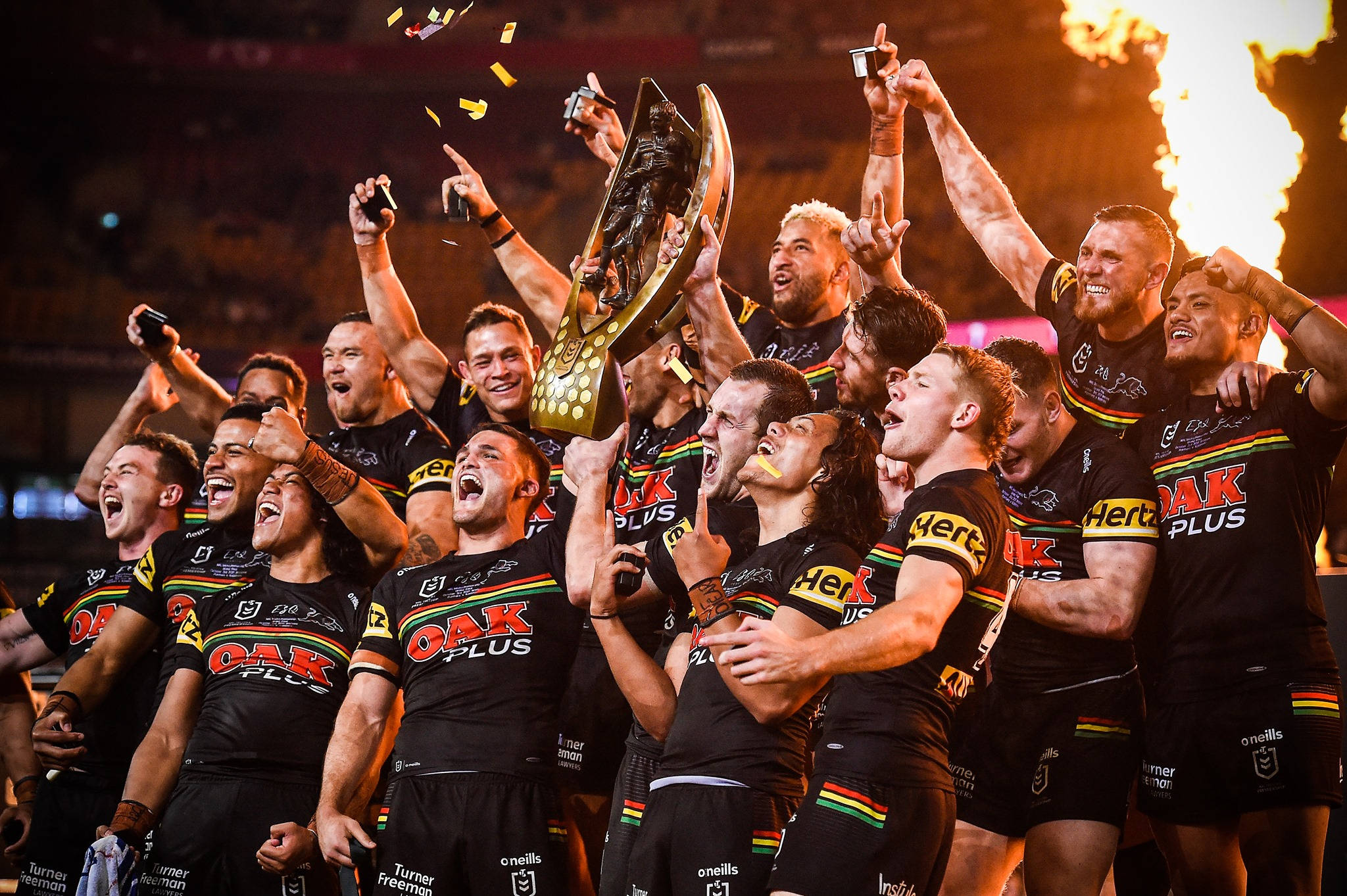 Nrl 桌布 壁紙 — 身穿黑色球衣的橄欖球聯賽球員瘋狂慶祝，手持金色獎盃，彩紙紛飛，身後火焰噴射。