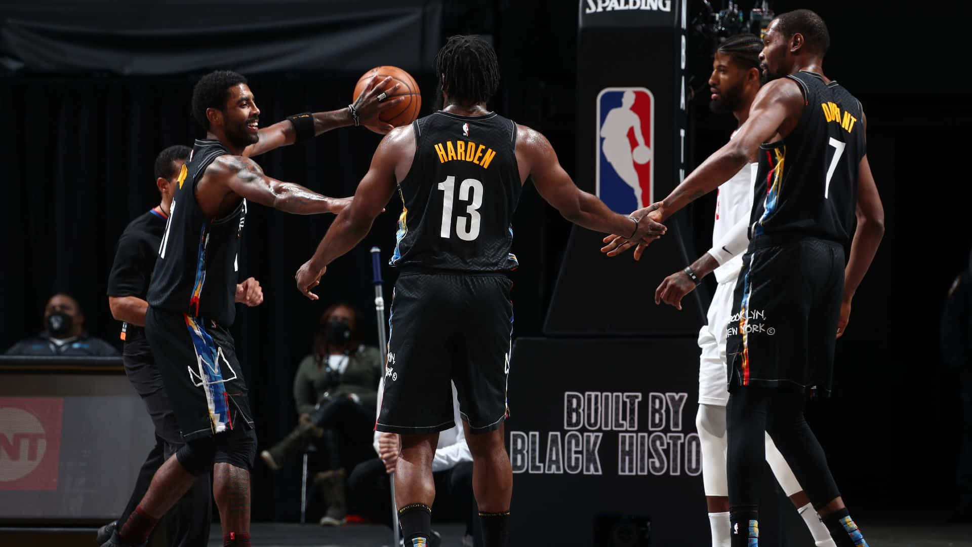 Brooklyn Nets 桌布 壁紙 — 身穿黑色球衣的籃球運動員在場館燈光下擊掌歡笑慶祝比賽。