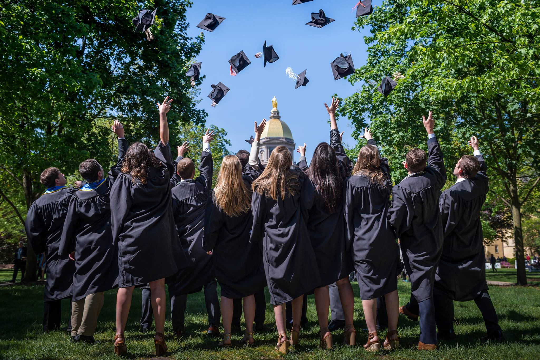 Graduation 桌布 壁紙 — 身穿黑色畢業袍的畢業生在晴朗的藍天下，背景有圓頂建築，歡欣地將畢業帽拋向天空。