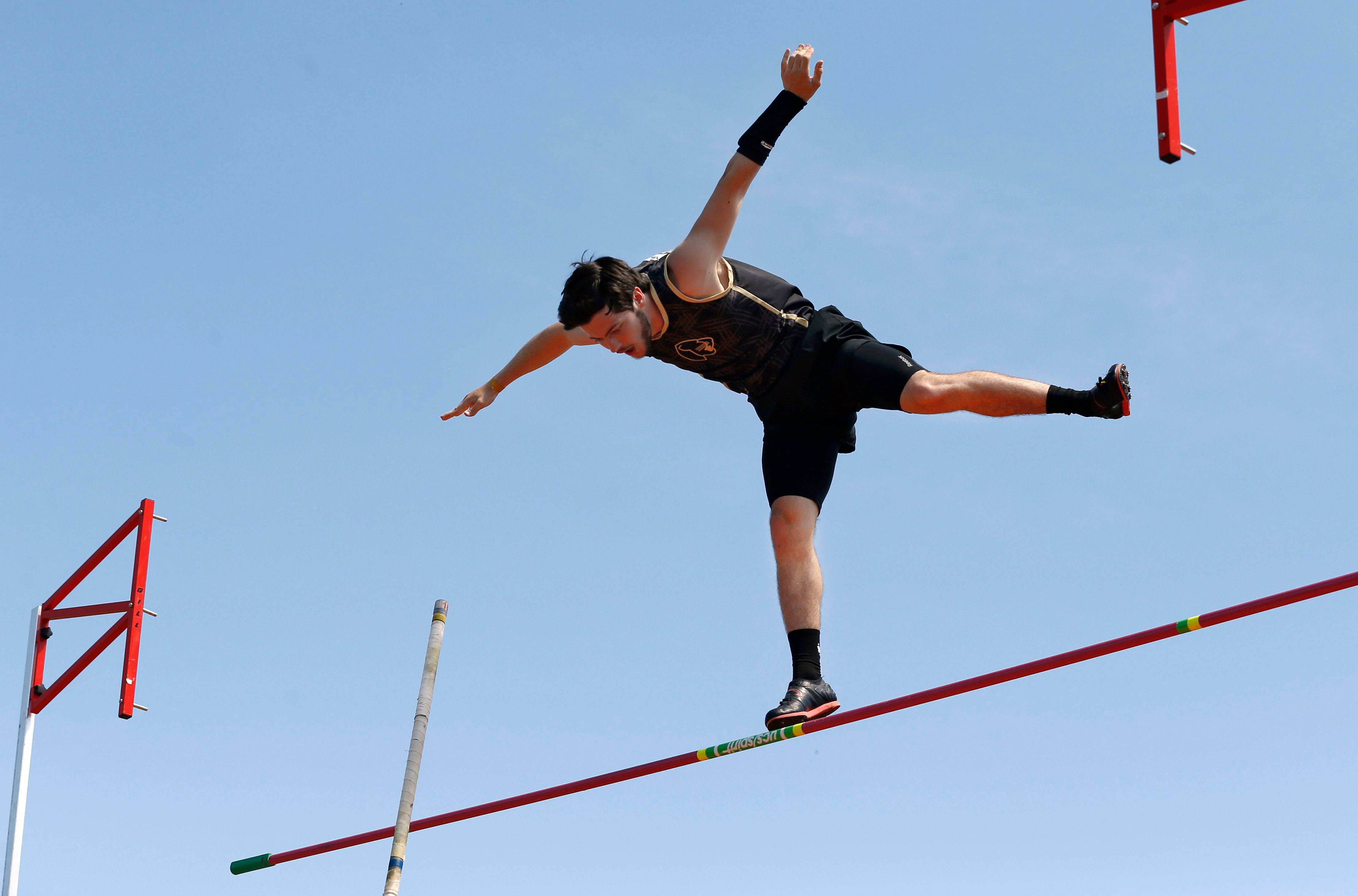 Athletic 桌布 壁紙 — 身穿黑色運動服的運動員在晴朗藍天下張開雙臂越過跳高橫桿。