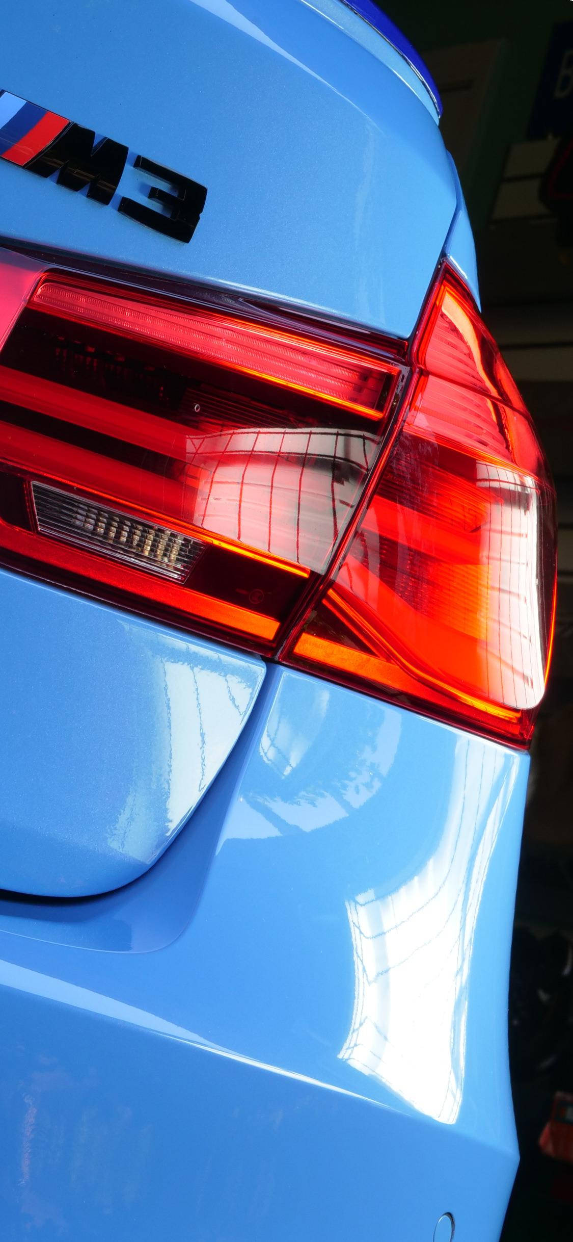 iPhone 桌布 壁紙 — 車庫中發紅光的亮面淺藍色BMW M3尾燈特寫。