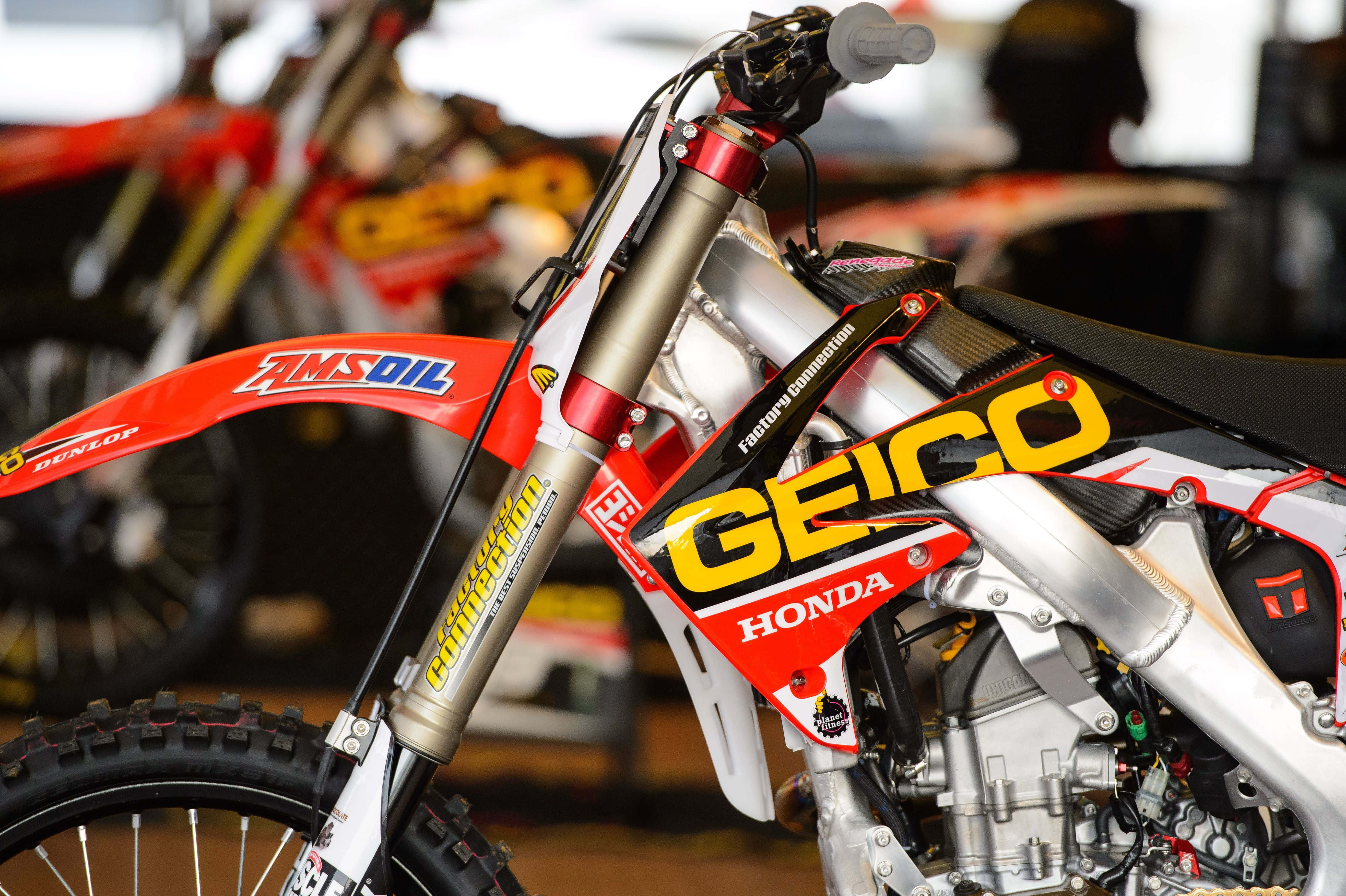 Honda Dirt Bike 桌布 壁紙 — 車庫中紅色和白色本田越野摩托車的特寫，帶有GEICO和AMSOIL品牌標誌。