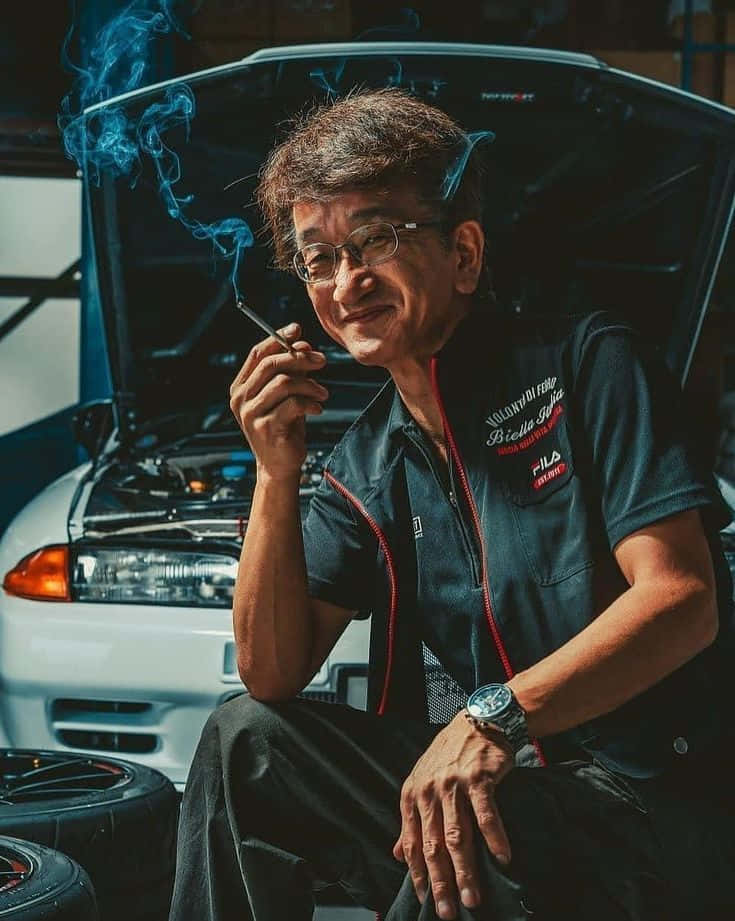 人像動態 桌布 壁紙 — 車庫裡一位微笑的機械師，坐在一輛打開引擎蓋的白色汽車前抽煙。