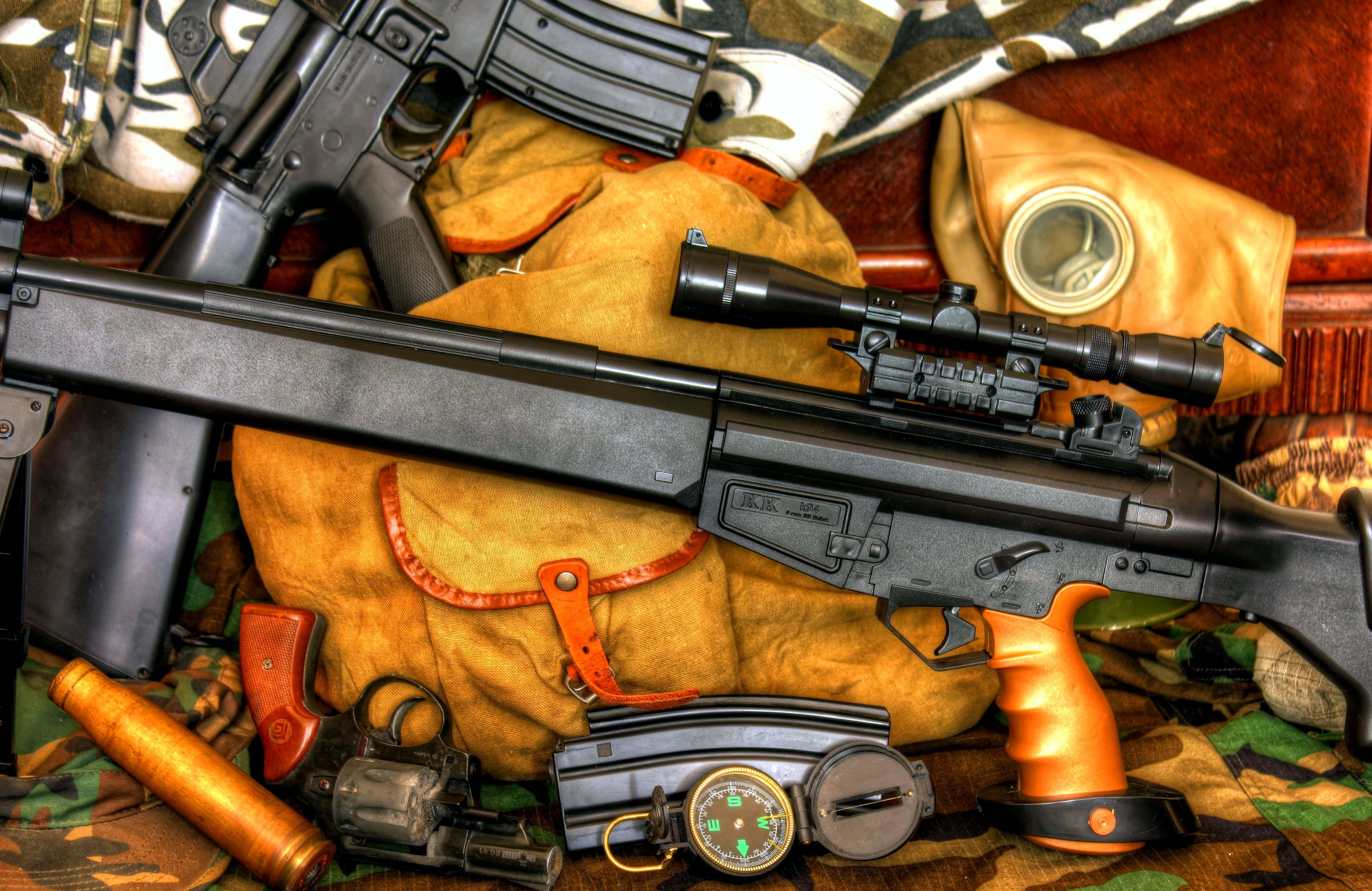 Rifle 桌布 壁紙 — 軍事裝備的特寫，包括步槍瞄準鏡和防毒面具，排列在迷彩布料上。