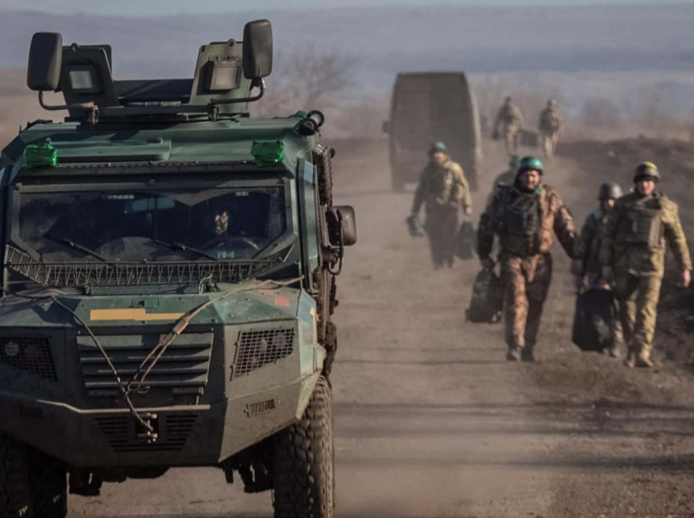 戰爭動圖 桌布 壁紙 — 軍事車隊，裝甲車和士兵在多雲的天空下穿越塵土飛揚的地形行進。