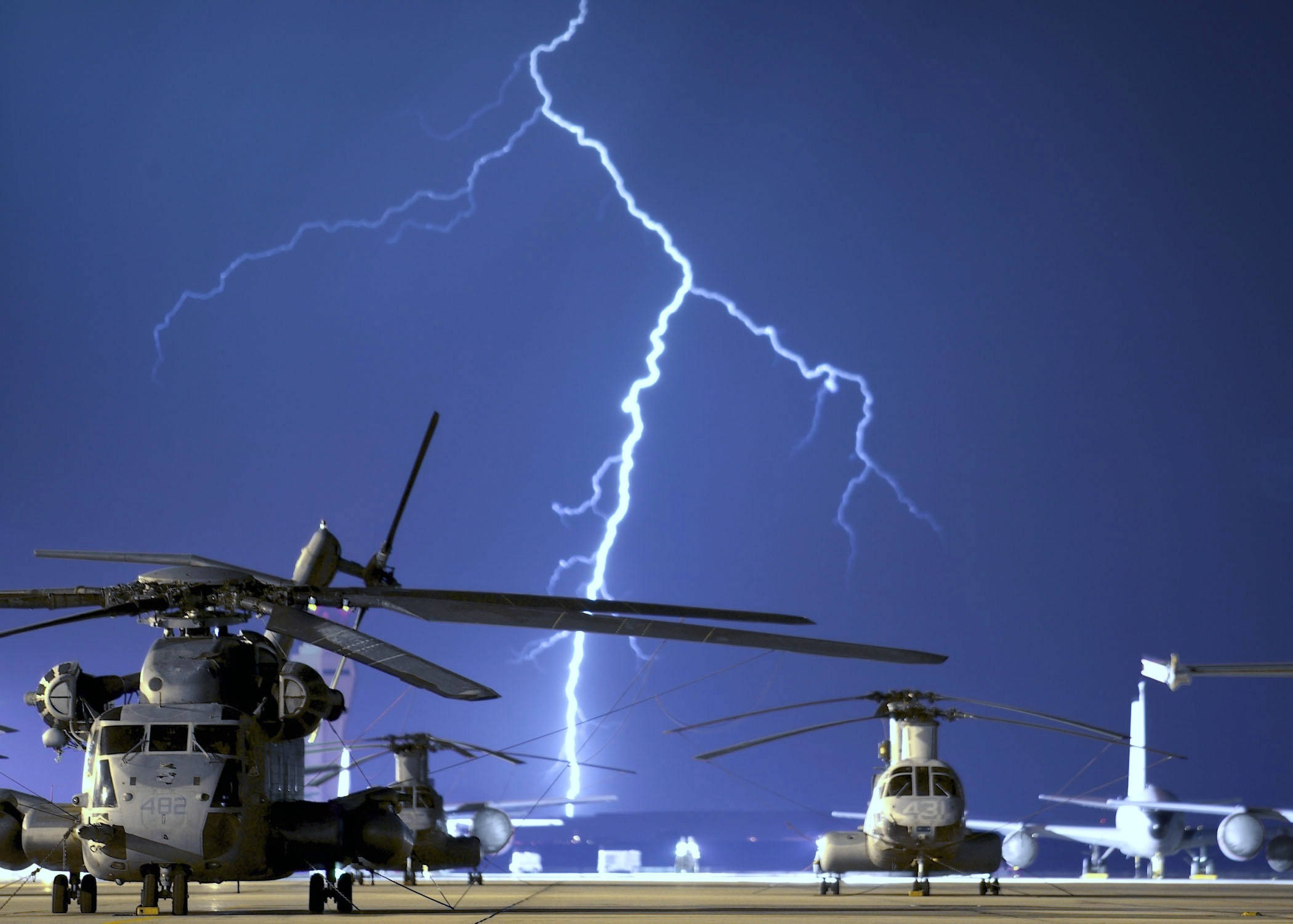 Helicopter 桌布 壁紙 — 軍用直升機靜止不動地停在機場上，一道巨大的閃電劃破上方深藍色的天空。