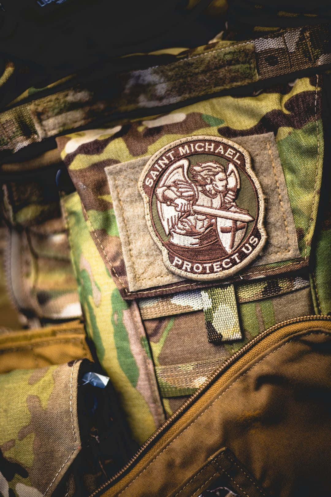 Saint Michael 桌布 壁紙 — 軍用迷彩背心上聖米迦勒徽章的近距離特寫，帶有精細刺繡和紋理布料。