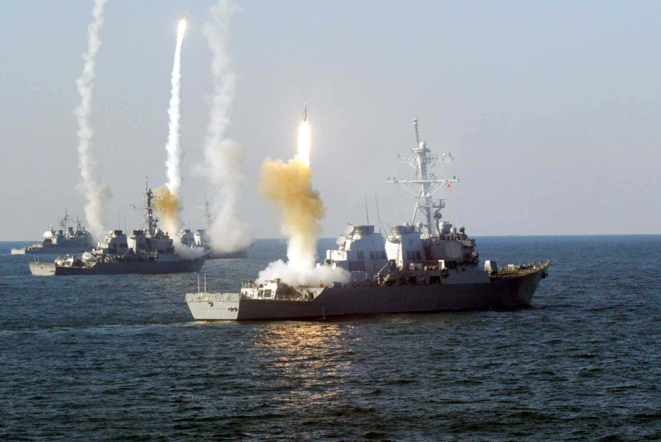 Navy 桌布 壁紙 — 軍艦在晴朗的天空下，在廣闊的海洋上齊射導彈，留下煙霧和火焰的痕跡。