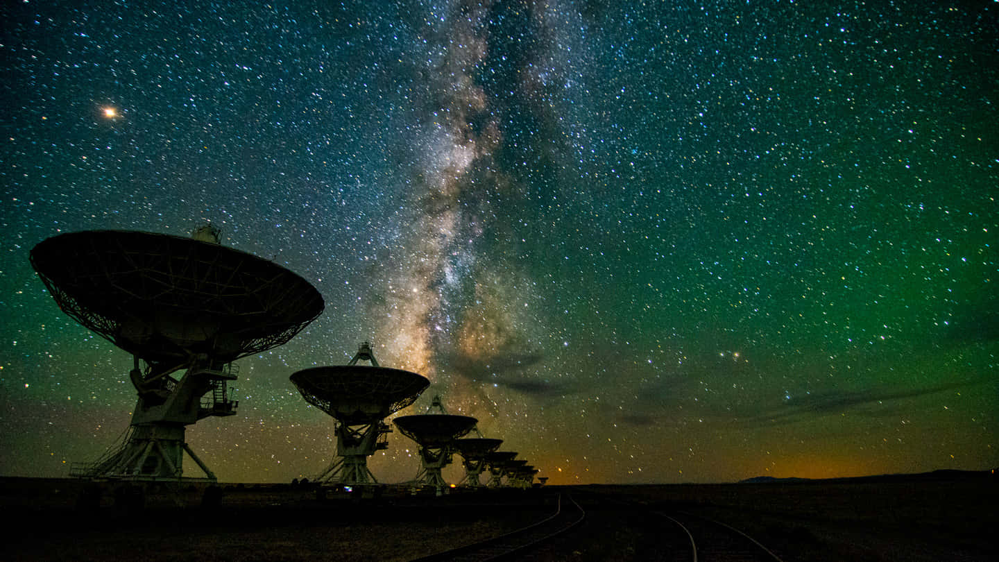 astronomy 桌布 壁紙 — 輪廓分明的無線電望遠鏡仰望充滿活力的星空，銀河系閃爍著綠色和藍色色調。